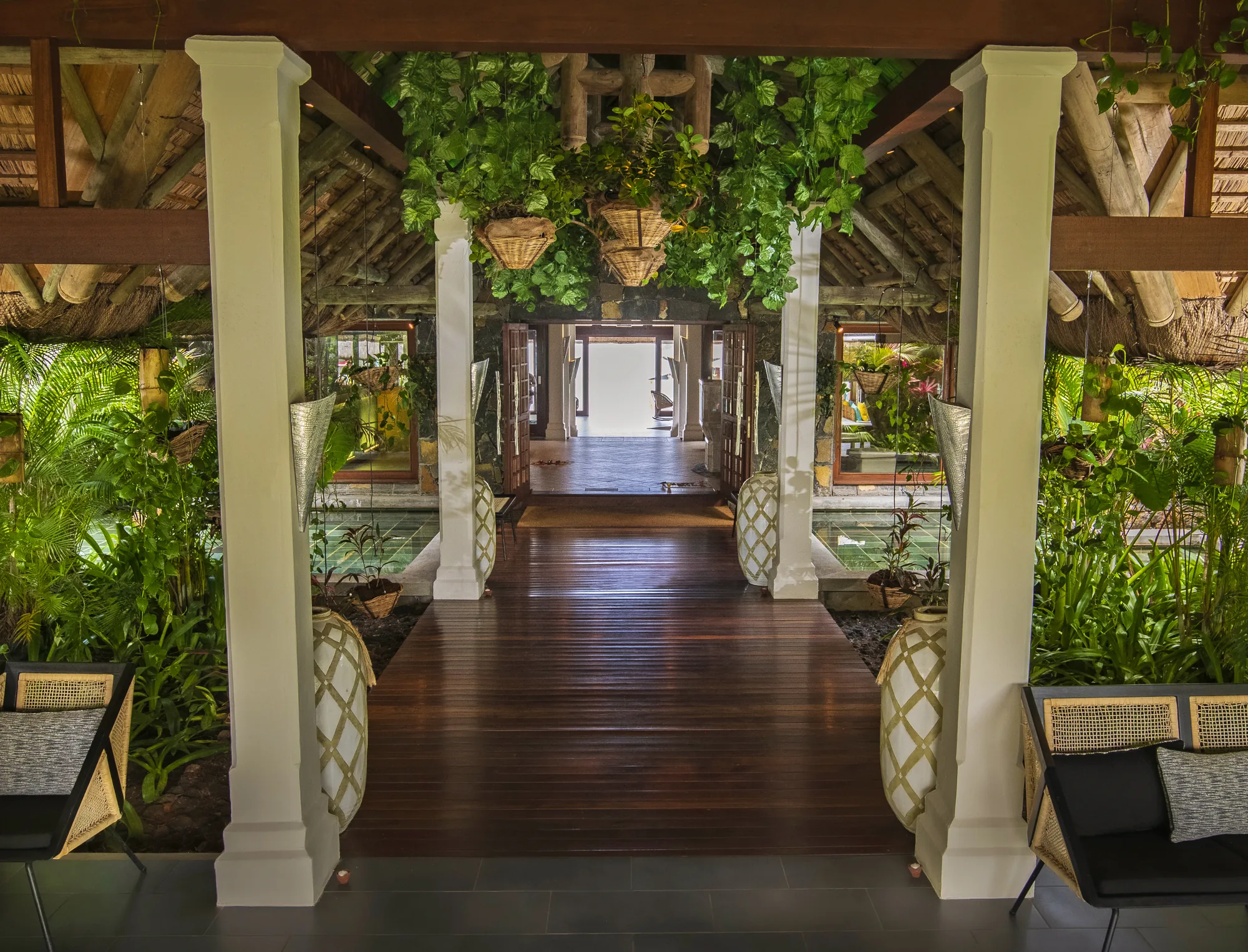 A timber walkway between columns, lined with hanging plants