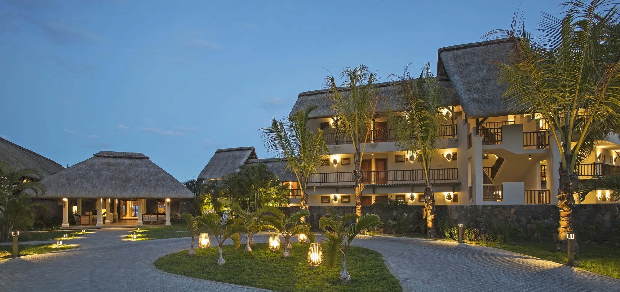 Thatched resort buildings lit at dusk along a curving driveway