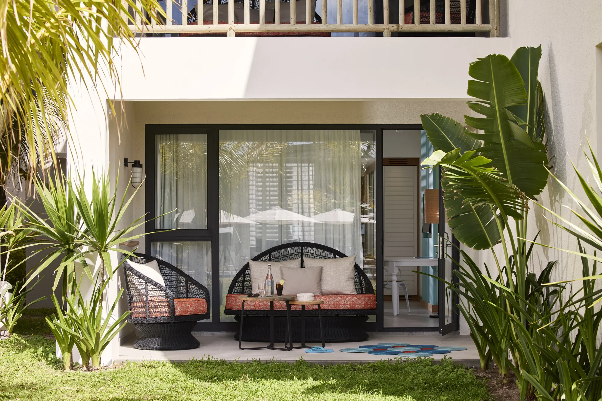 A ground floor terrace with woven chairs among tropical plants
