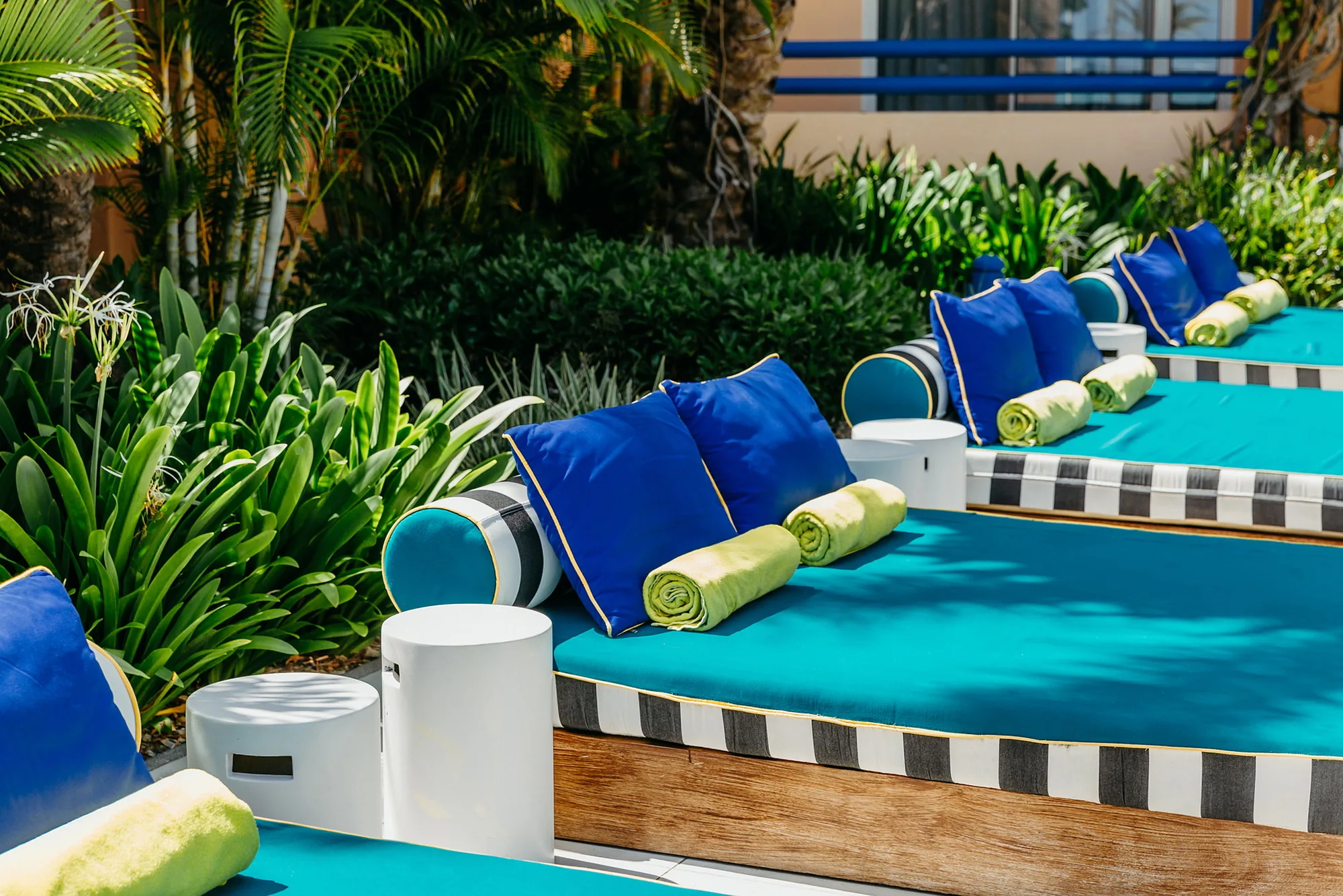 Daybeds with blue and turquoise cushions among tropical plants