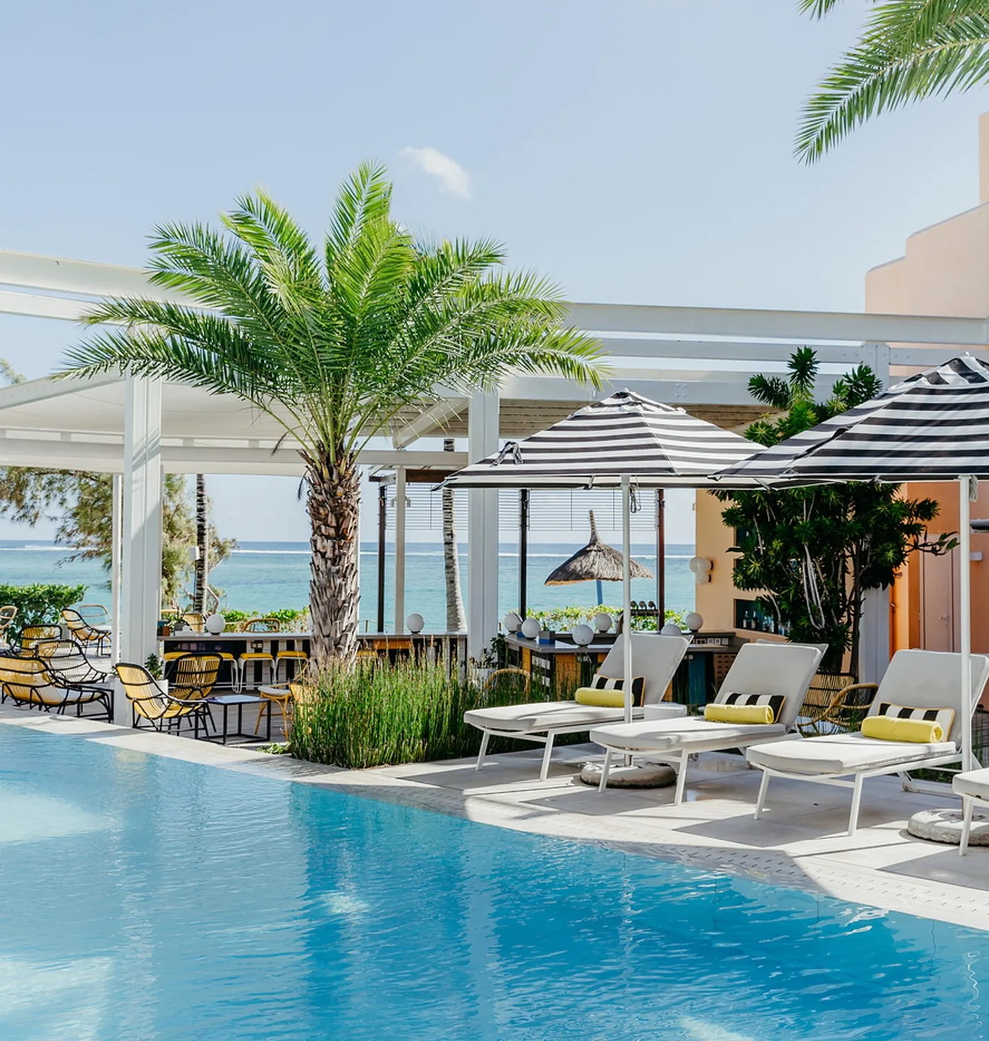 A pool with loungers and striped parasols in front of a white terrace bar