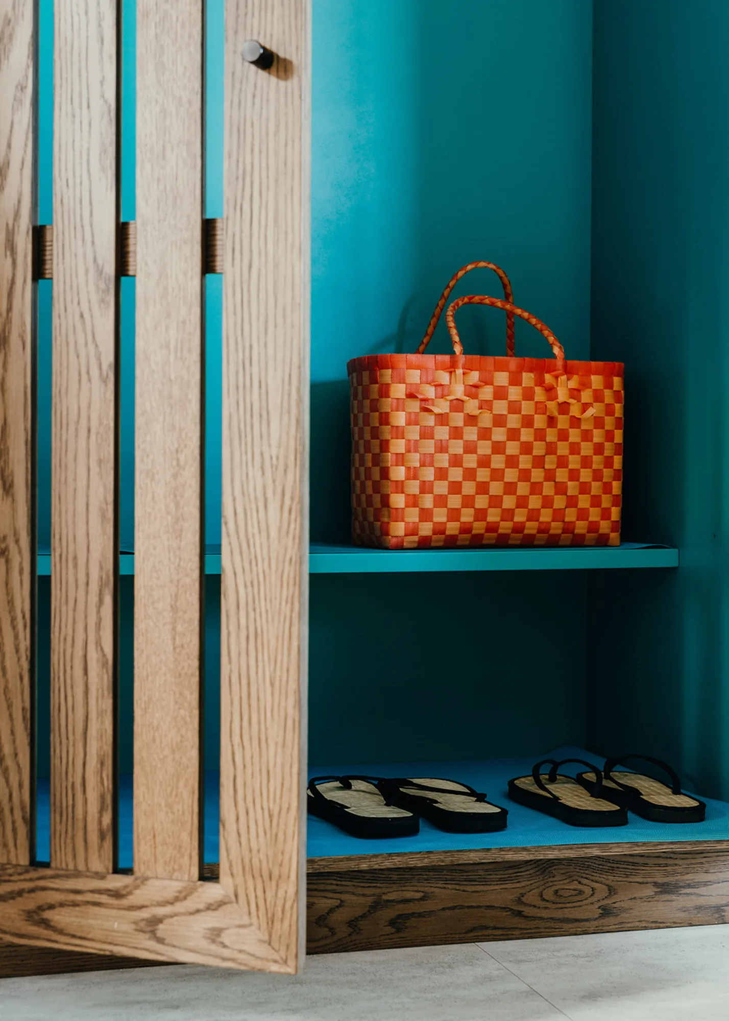 A turquoise wardrobe niche holding a woven basket and sandals