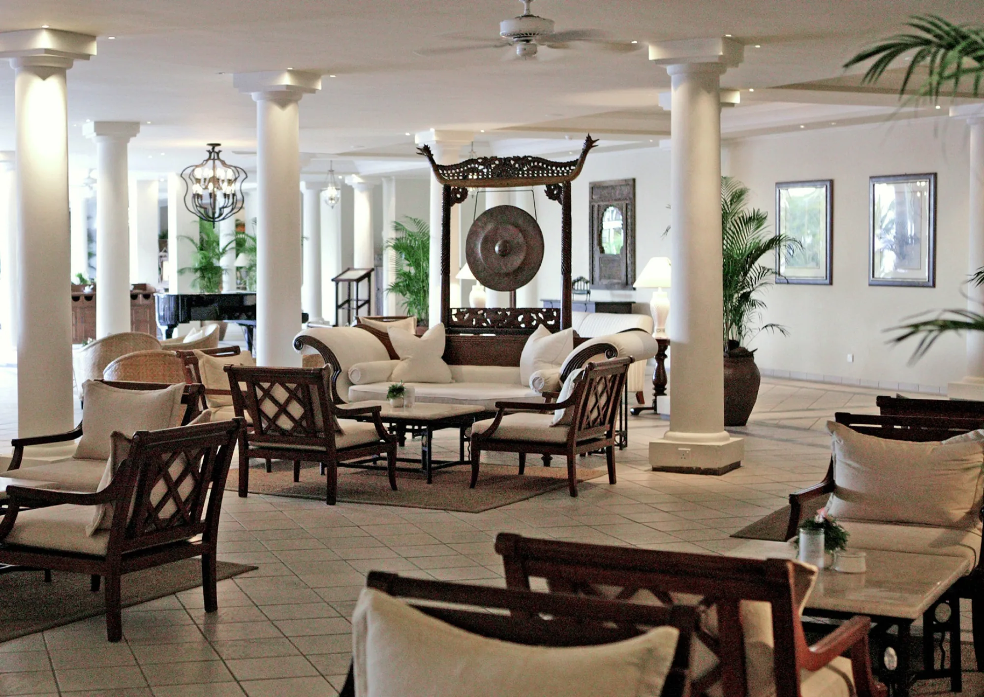 A lounge with white columns, wooden armchairs and a carved screen