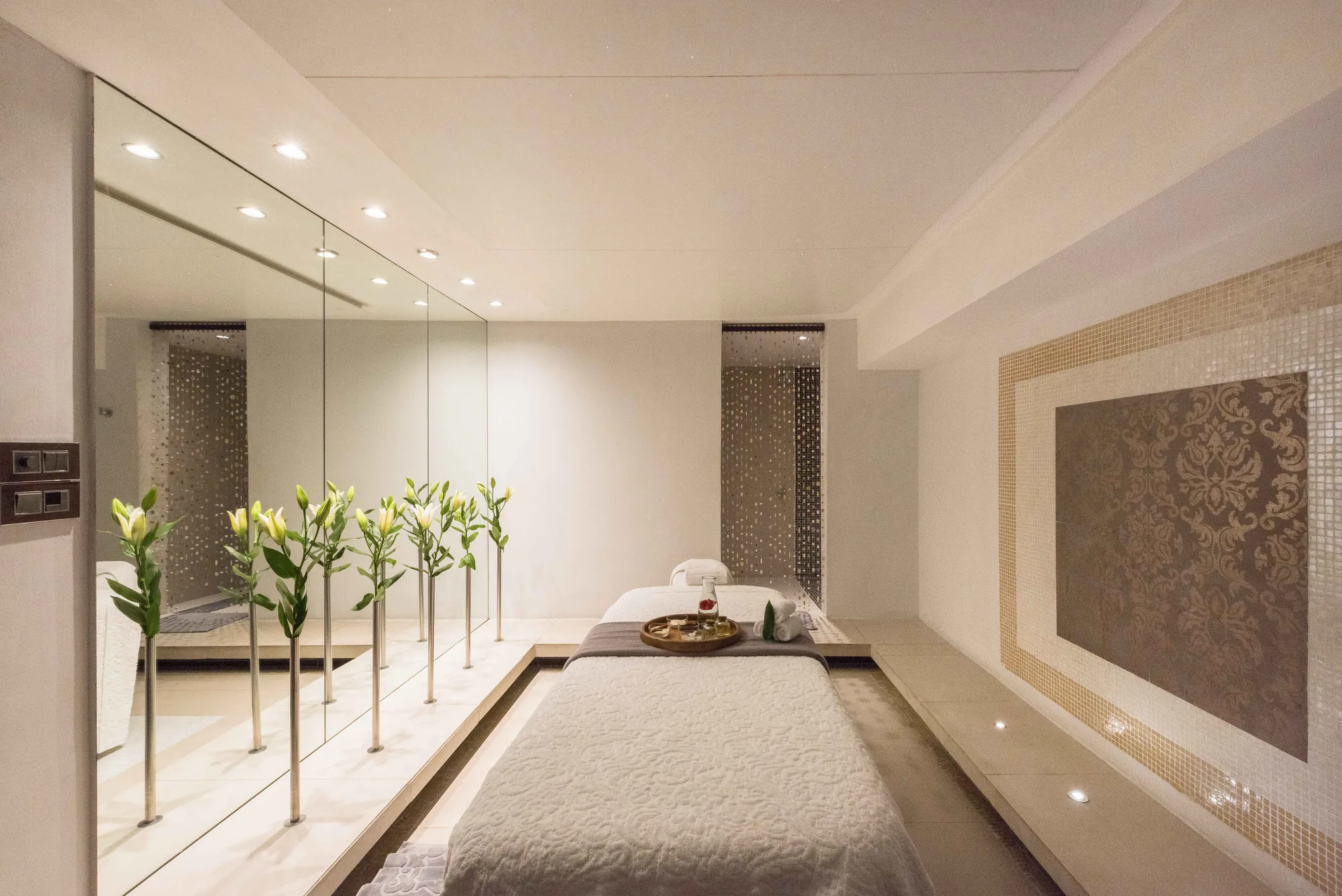 A spa treatment room with a massage table and white lilies along a mirrored wall