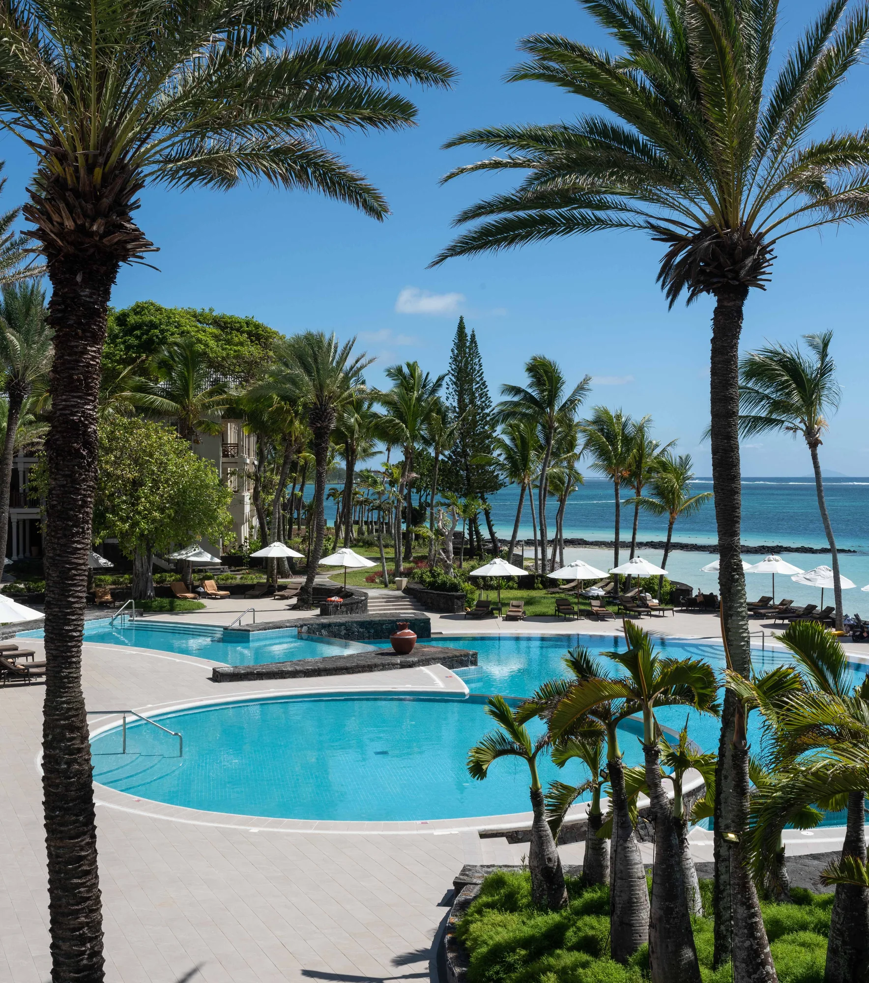 Pools among palm trees in front of the beach, seen from a balcony