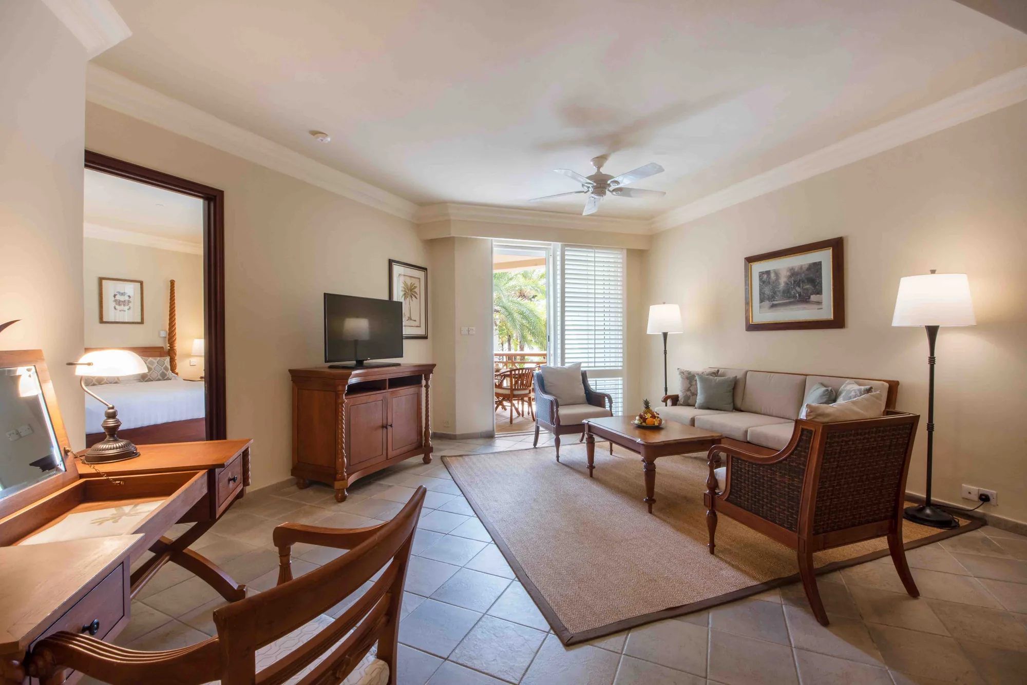 A suite sitting room with a sofa, a desk and doors open to a balcony