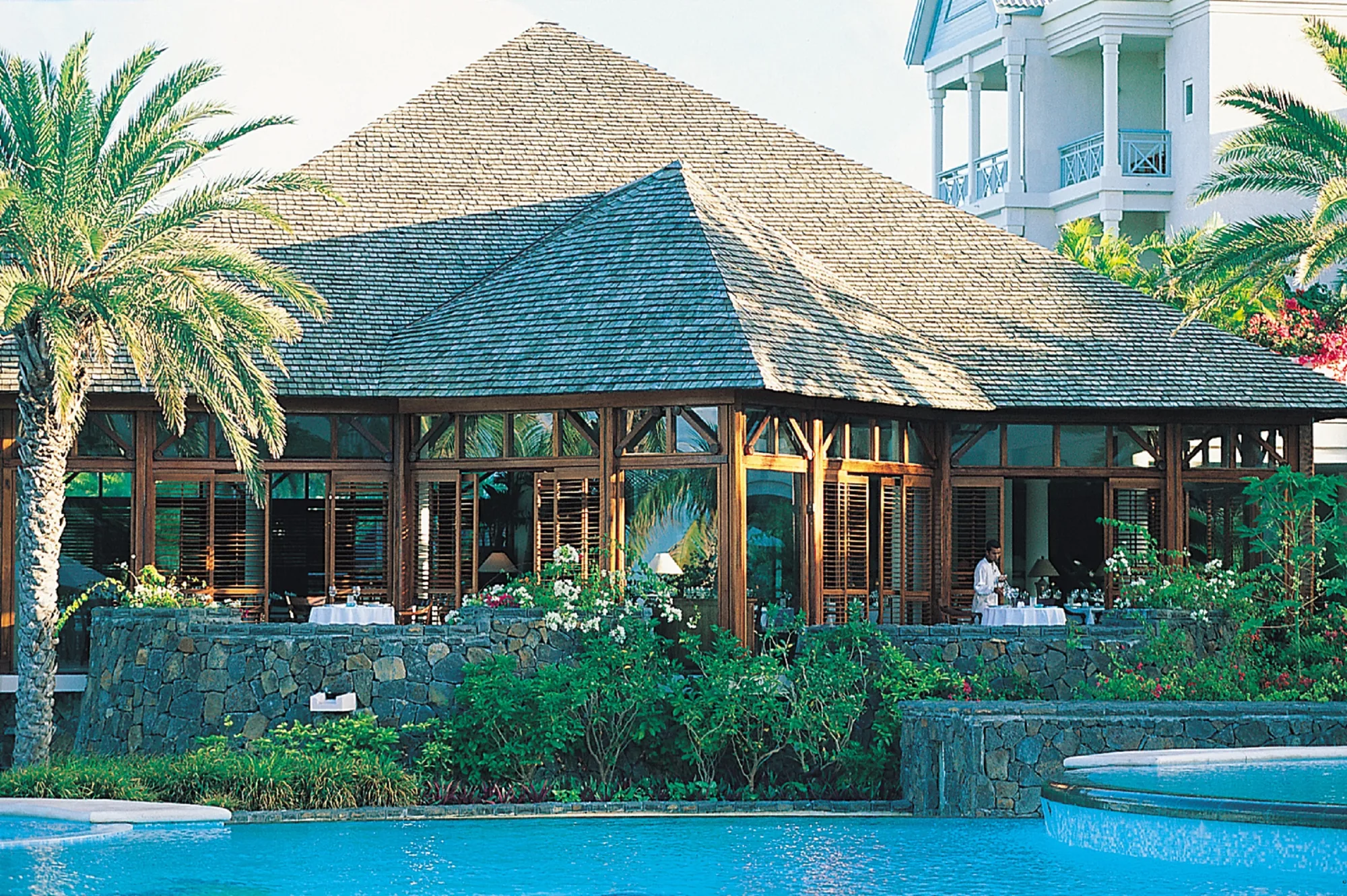 A restaurant under a pyramid roof beside the pool, among tropical gardens