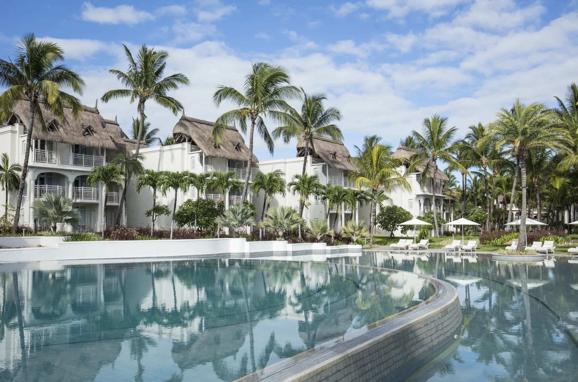 The long pool at LUX* Belle Mare, with white accommodation buildings and palm trees reflected in the water