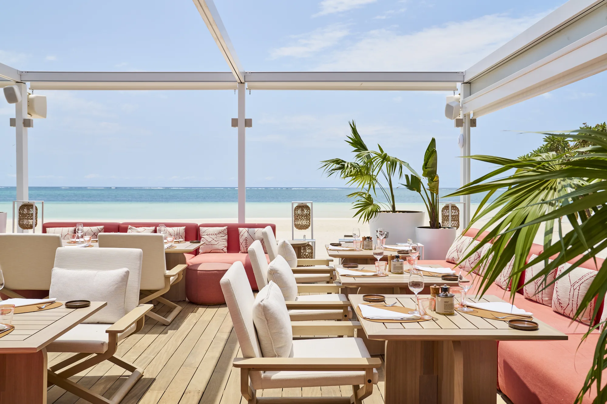 A beachside deck restaurant with white chairs and pink banquettes