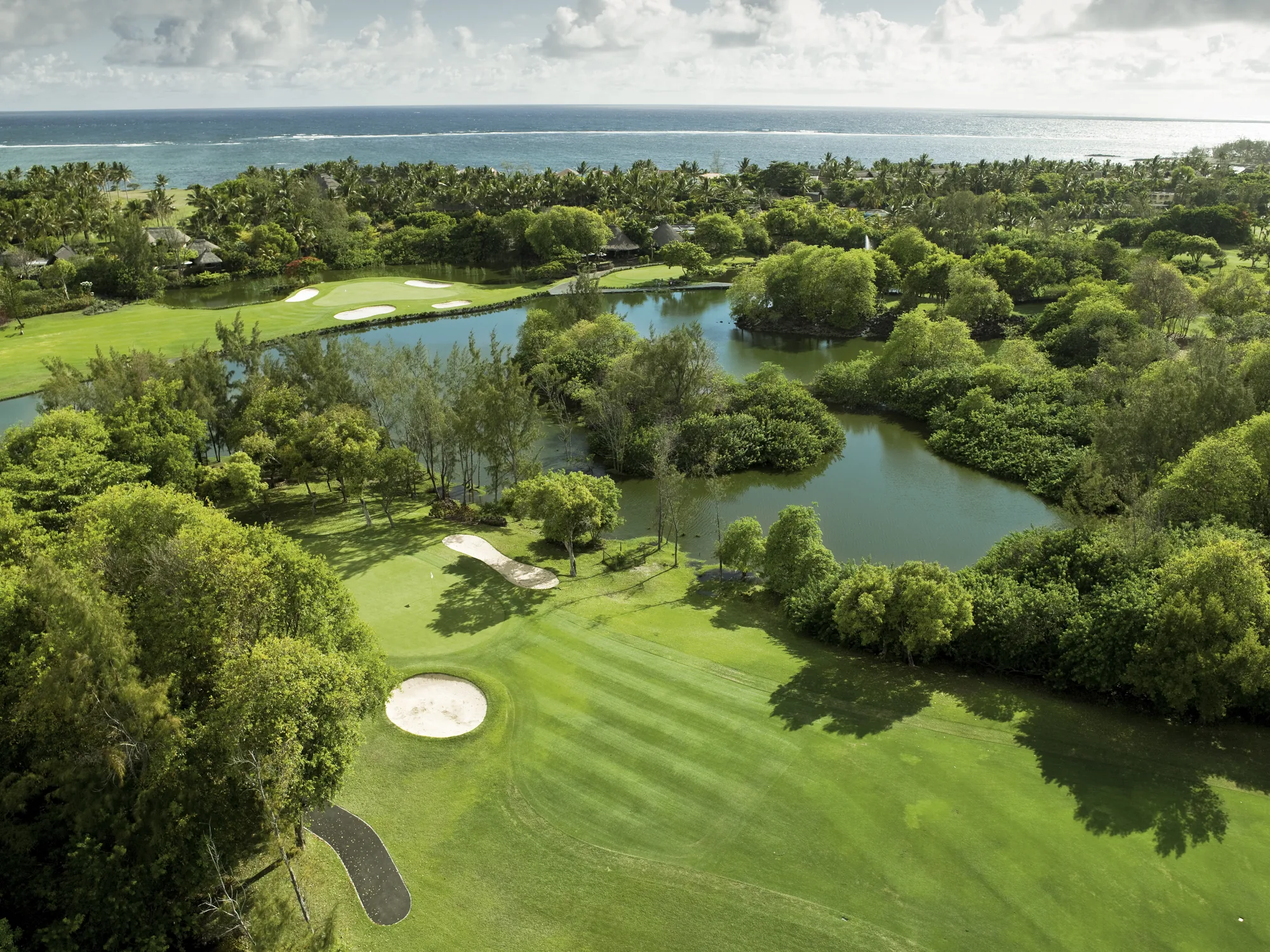 Aerial view of a golf fairway and lakes among green trees, with the sea beyond