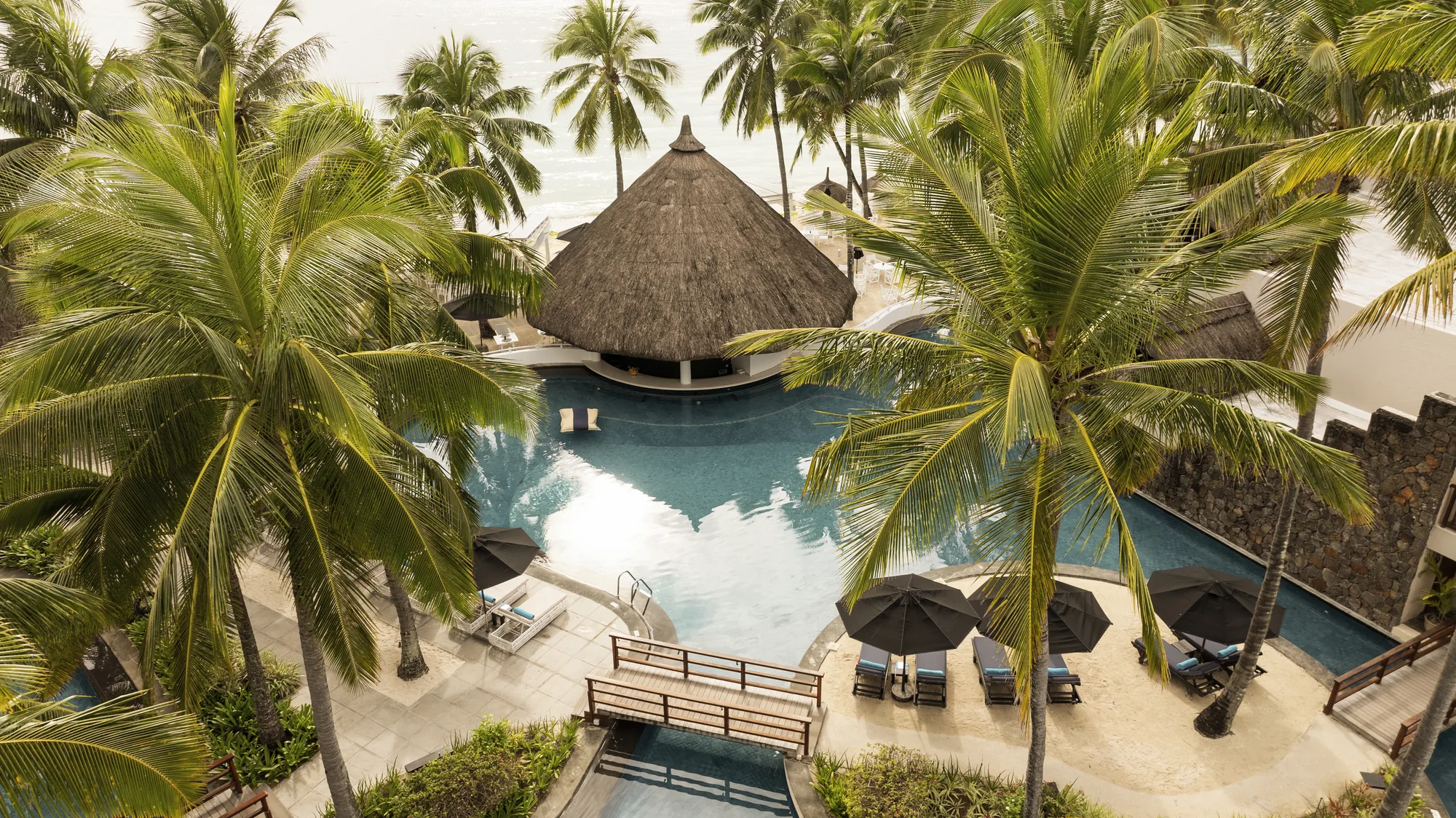A thatched pool bar in the middle of a pool, surrounded by palm trees