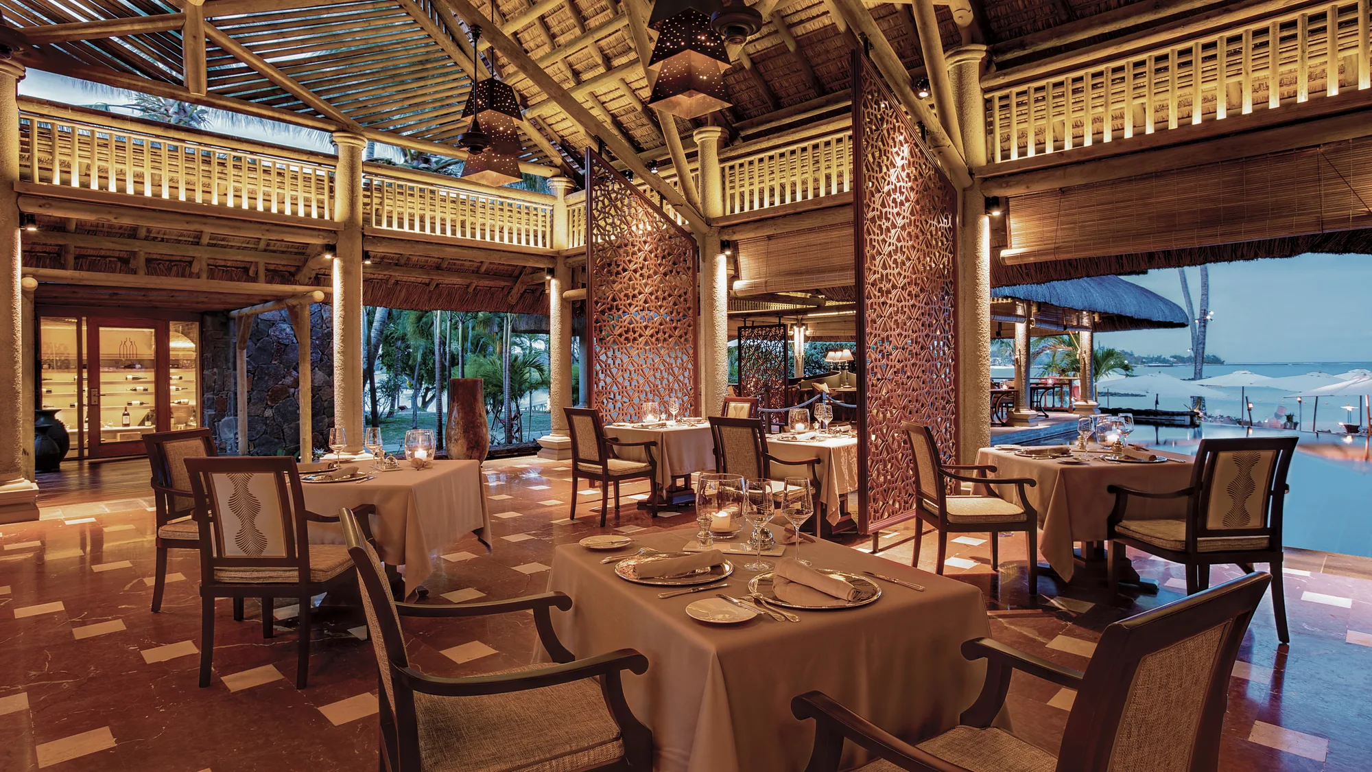 A restaurant with laid tables and carved timber screens, open to the sea