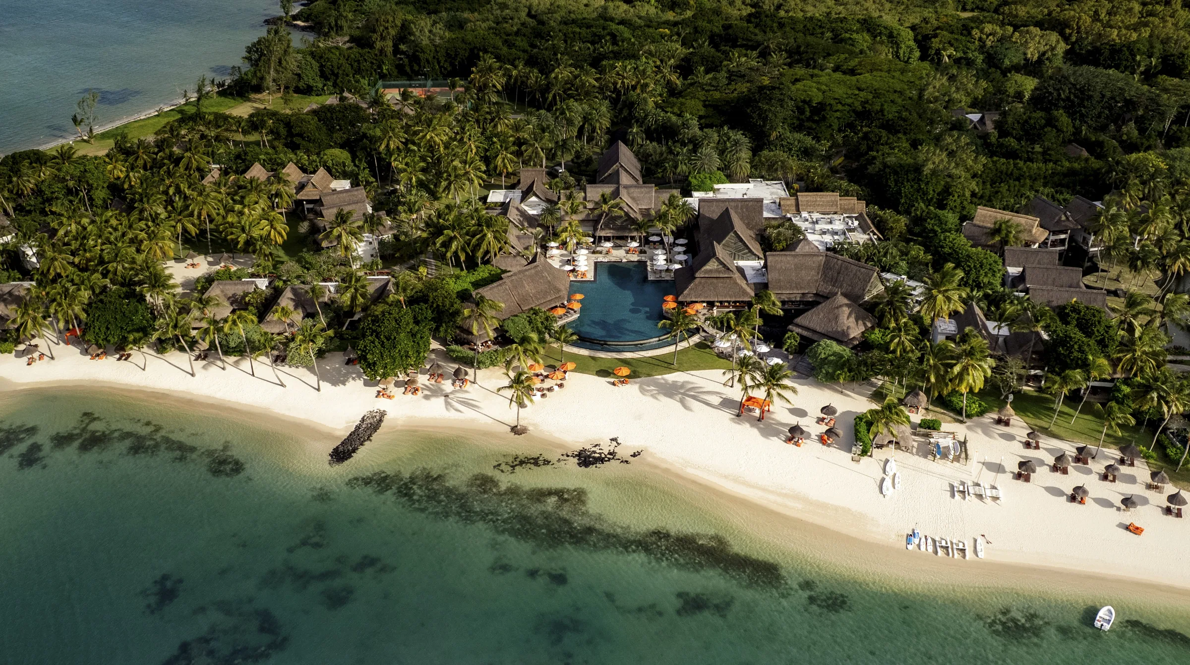 Aerial view of Constance Prince Maurice, its thatched roofs and pool among trees behind the beach