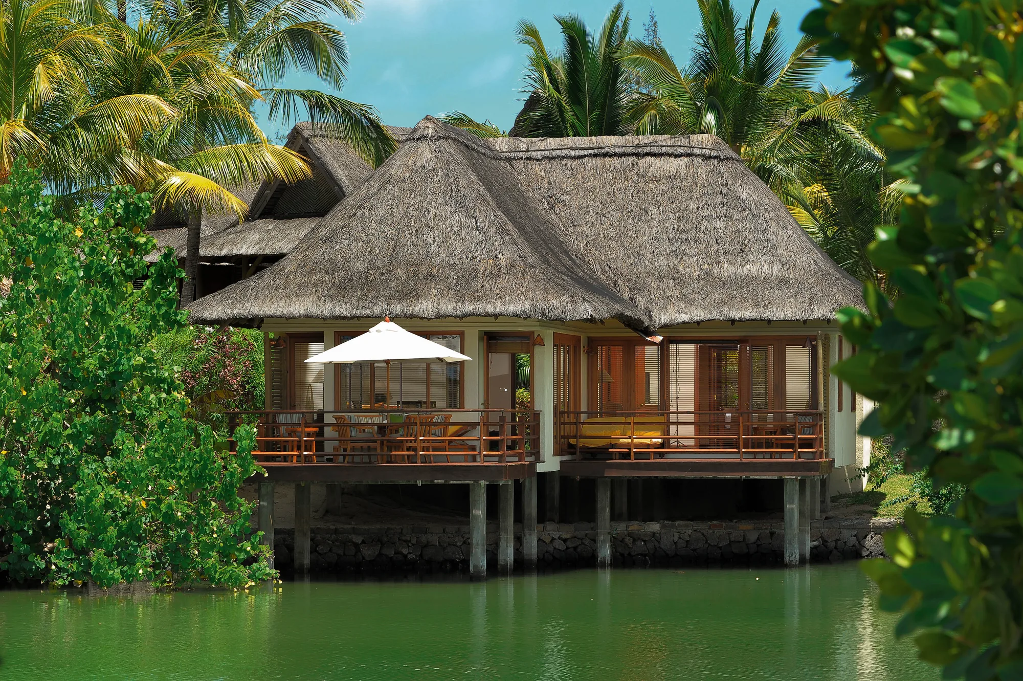 A thatched suite on stilts above green water, framed by trees