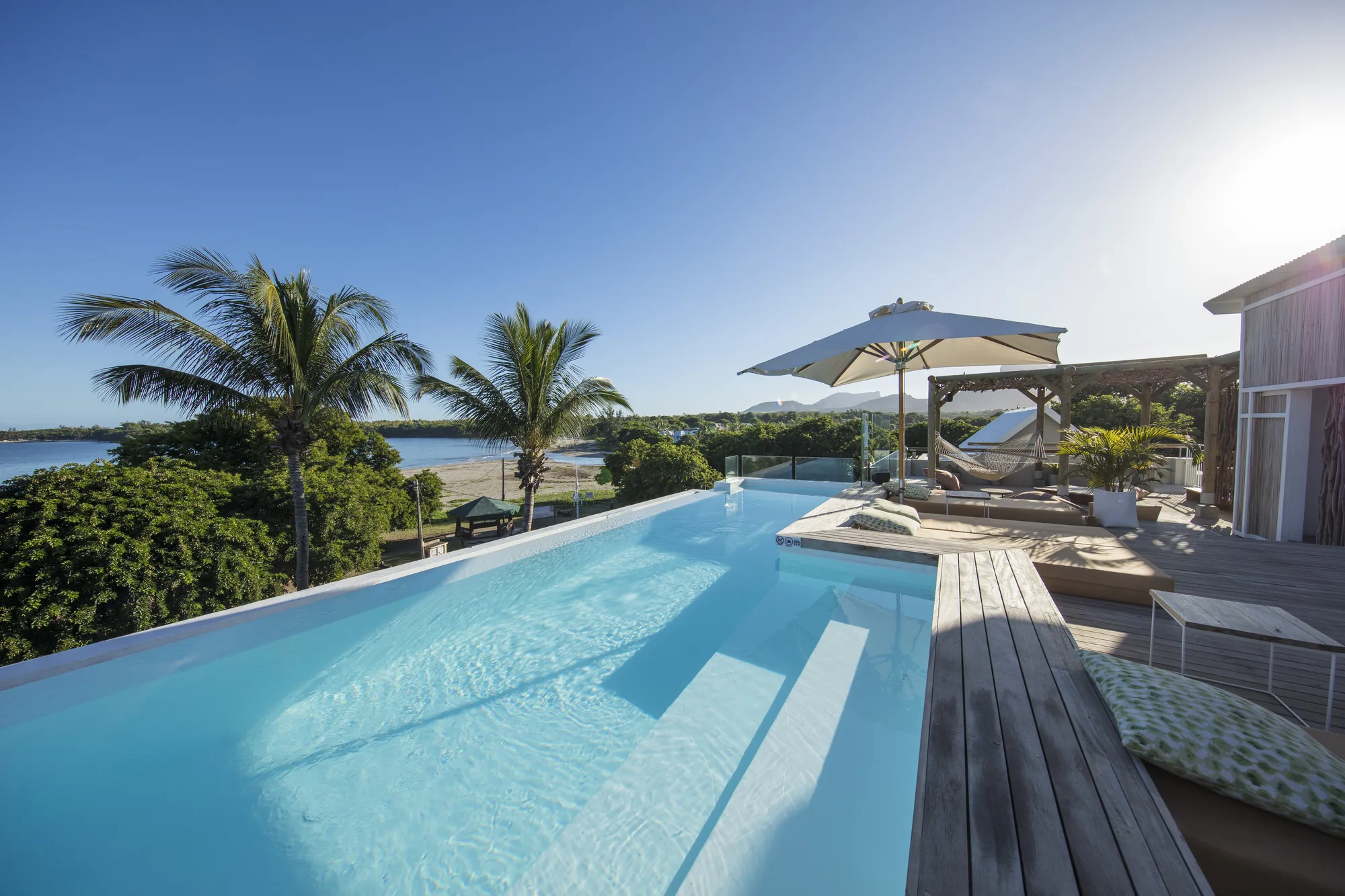 A rooftop infinity pool with a parasol and loungers, looking over the bay