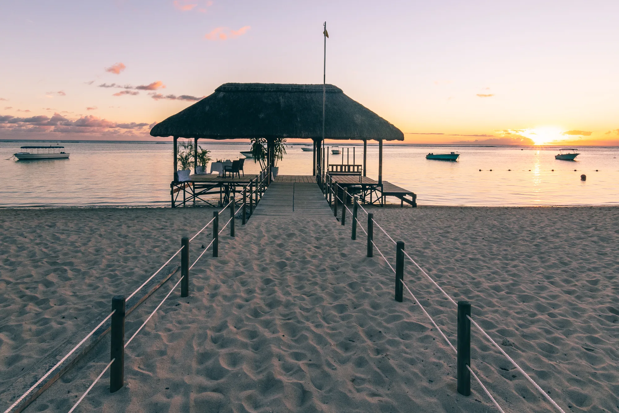 A jetty with a thatched pavilion at its end, at sunset