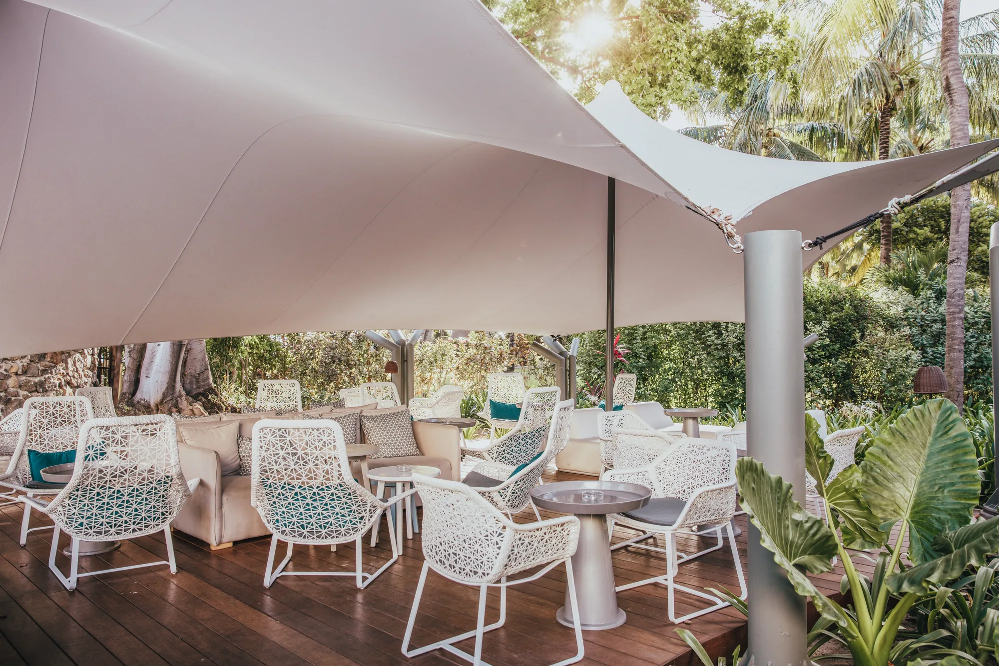 A terrace with white chairs and tables under shade sails