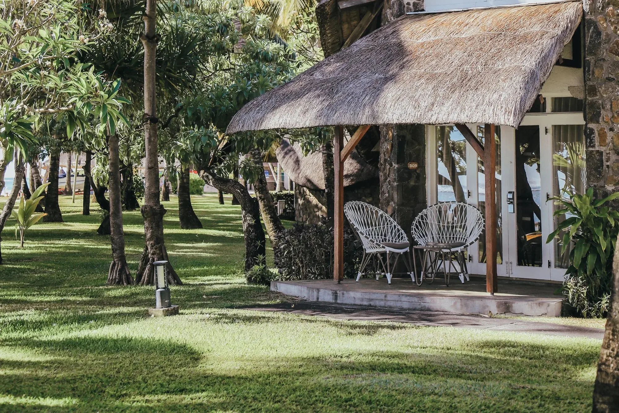 A thatched cottage terrace with white chairs, among trees on a lawn