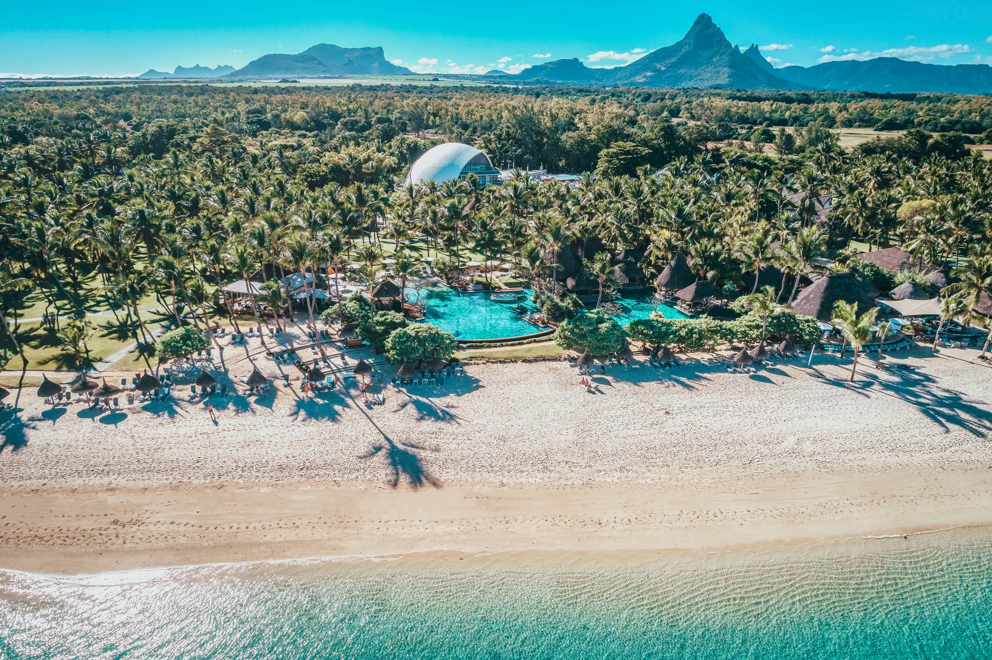 Aerial view of the beach, pool and palm groves, with mountains beyond