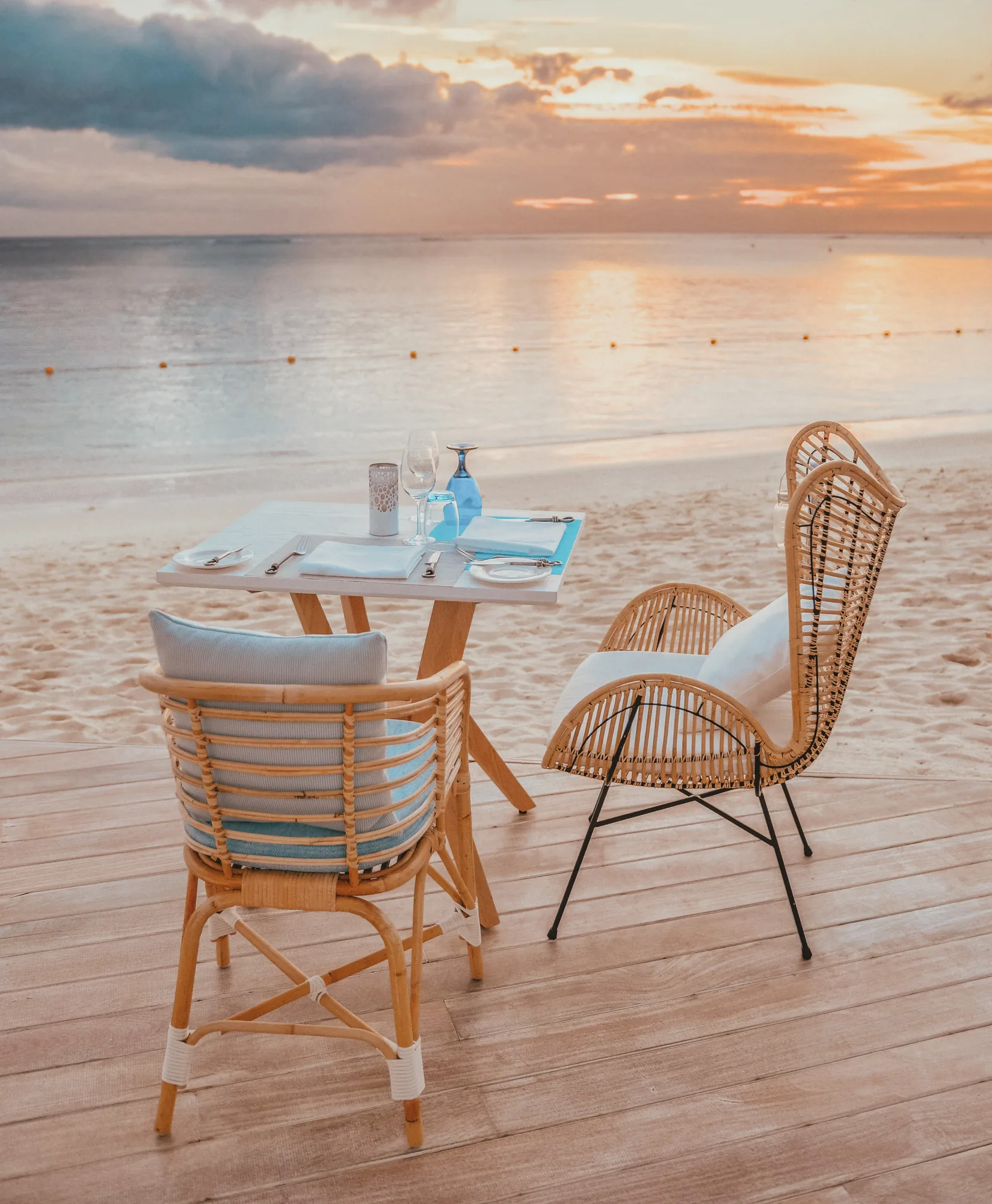 A small table and two rattan chairs on a deck by the sea at sunset