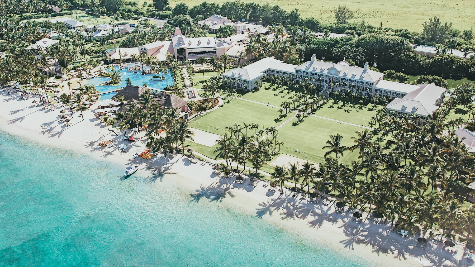 Aerial view of Sugar Beach, A Sunlife Resort, its manor house, lawns and pools behind the beach
