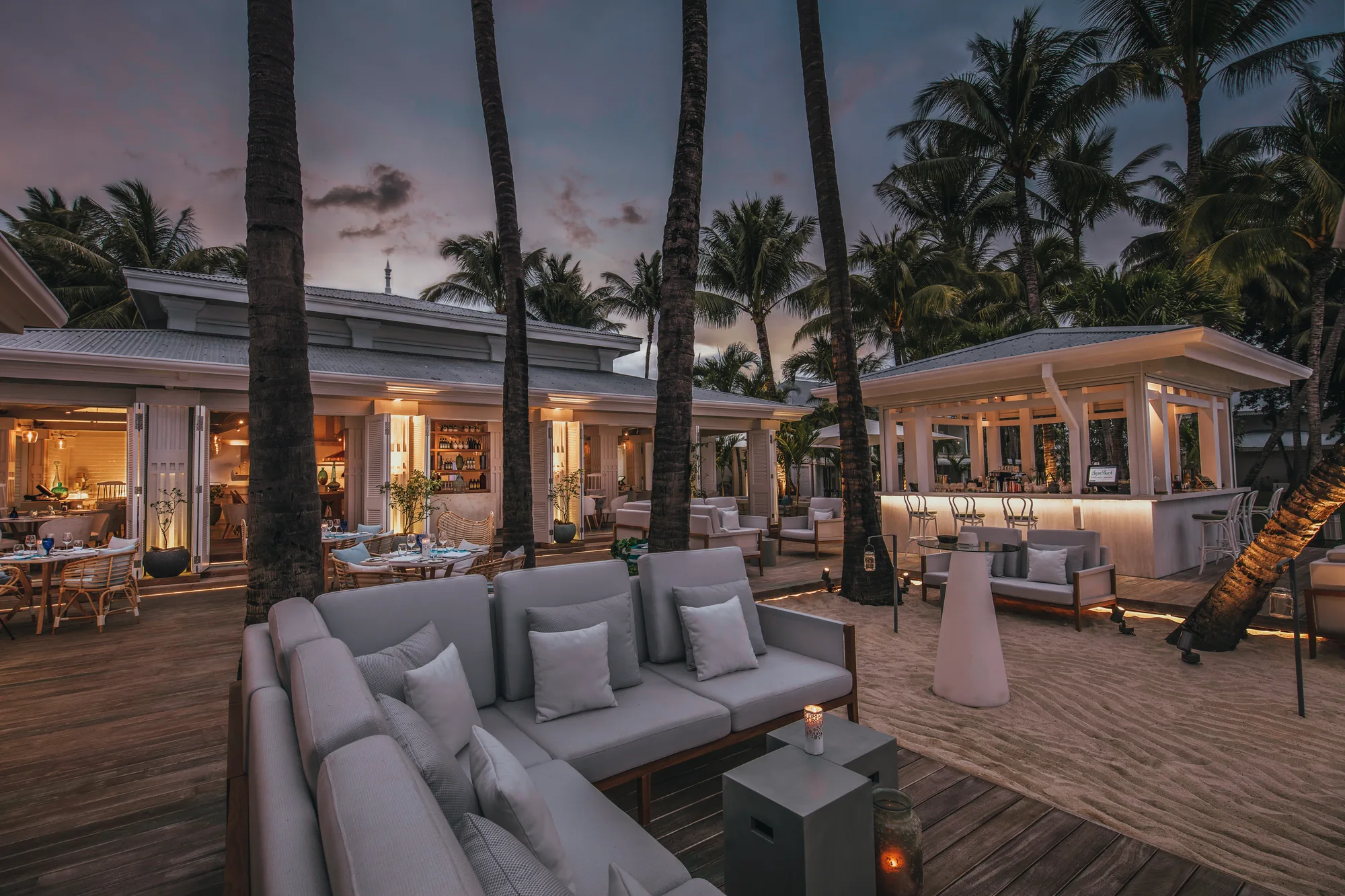 Outdoor sofas on a deck in front of lit restaurant pavilions at dusk