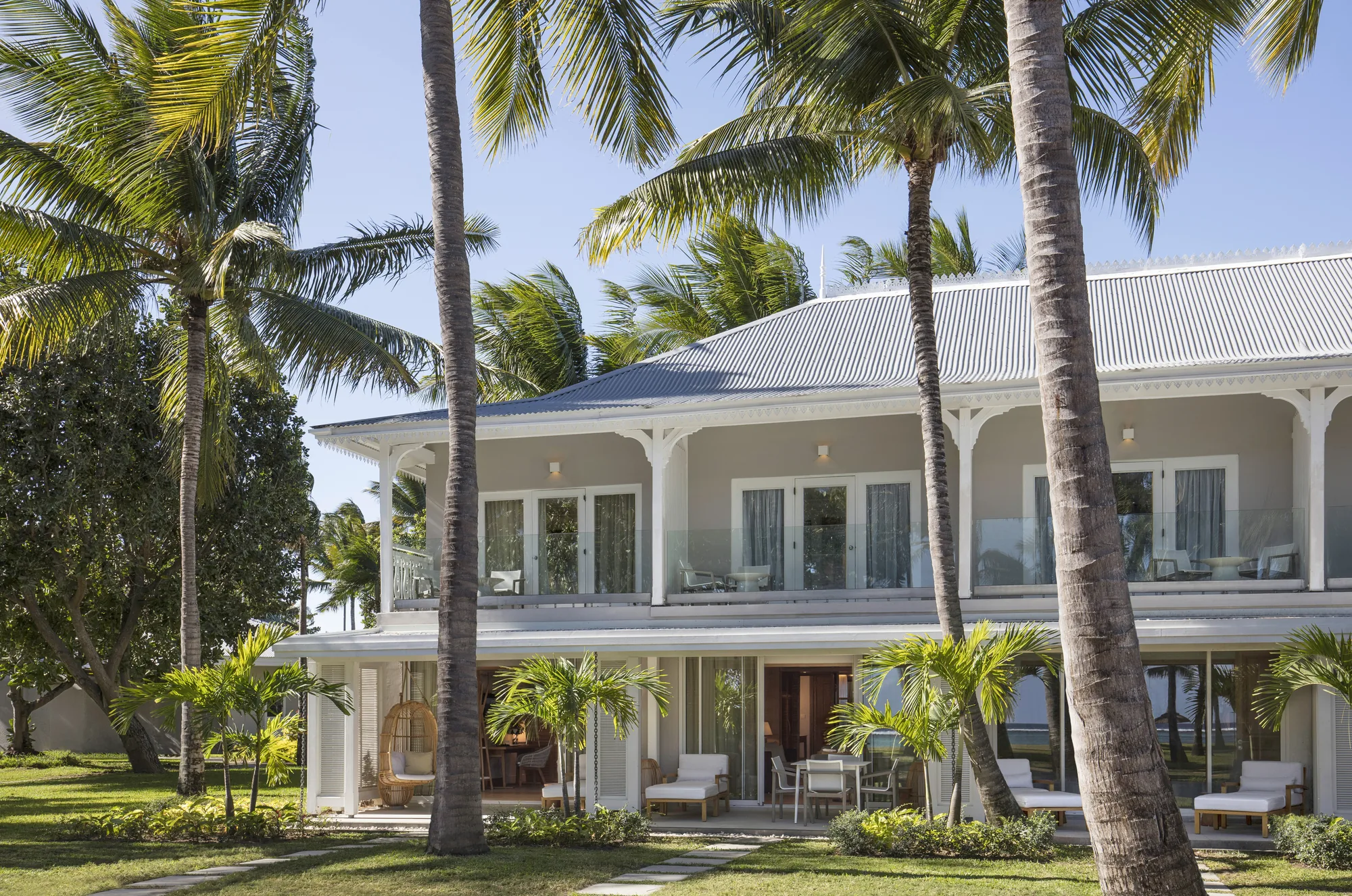 A two-storey colonial-style villa house with verandas, among palm trees
