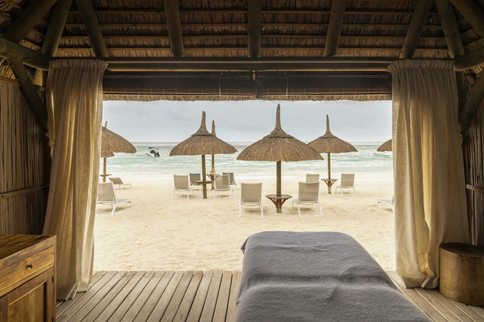 A spa pavilion with a massage table, open to the beach and parasols