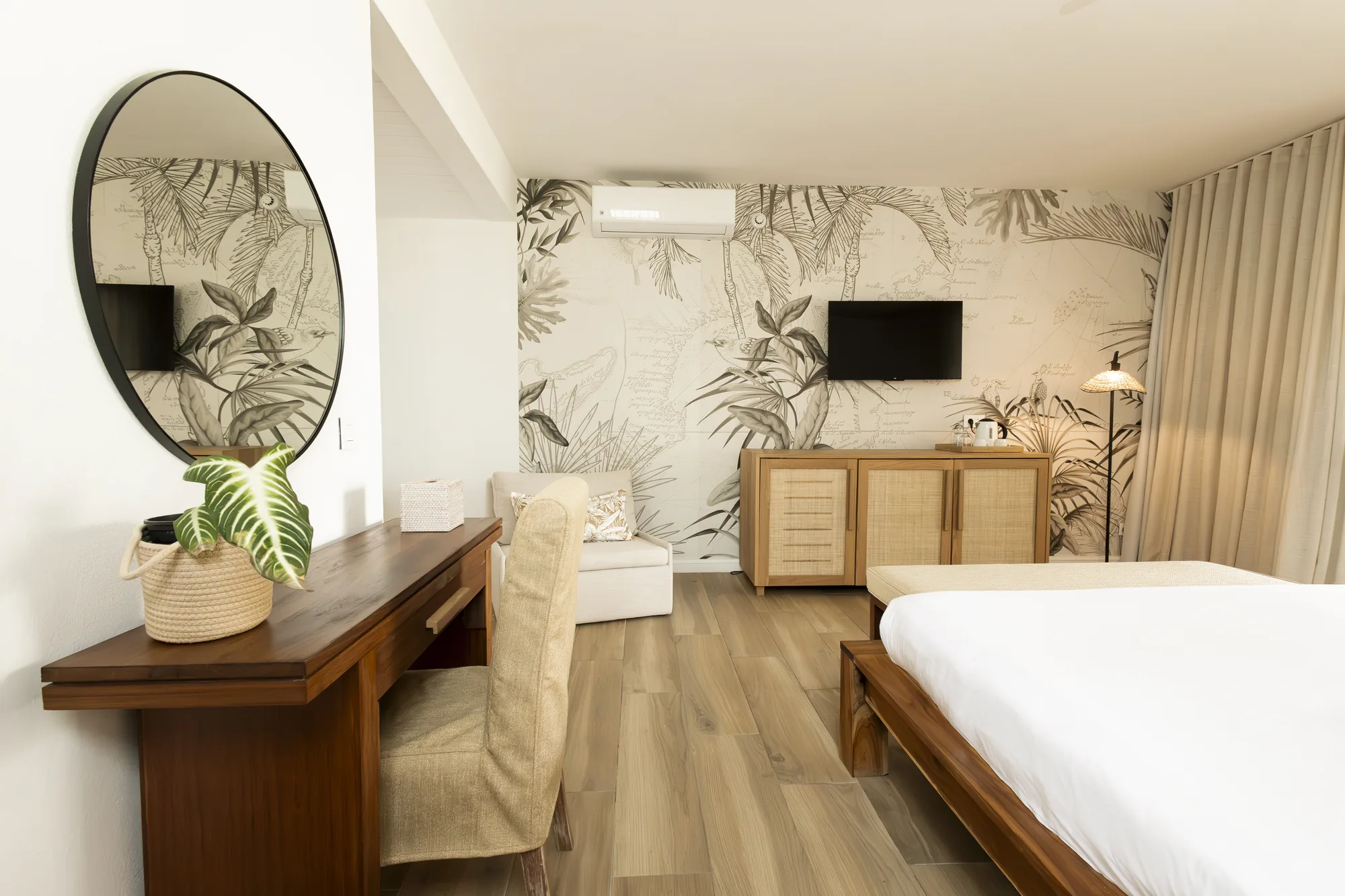 A bedroom with botanical wallpaper, a round mirror and a writing desk