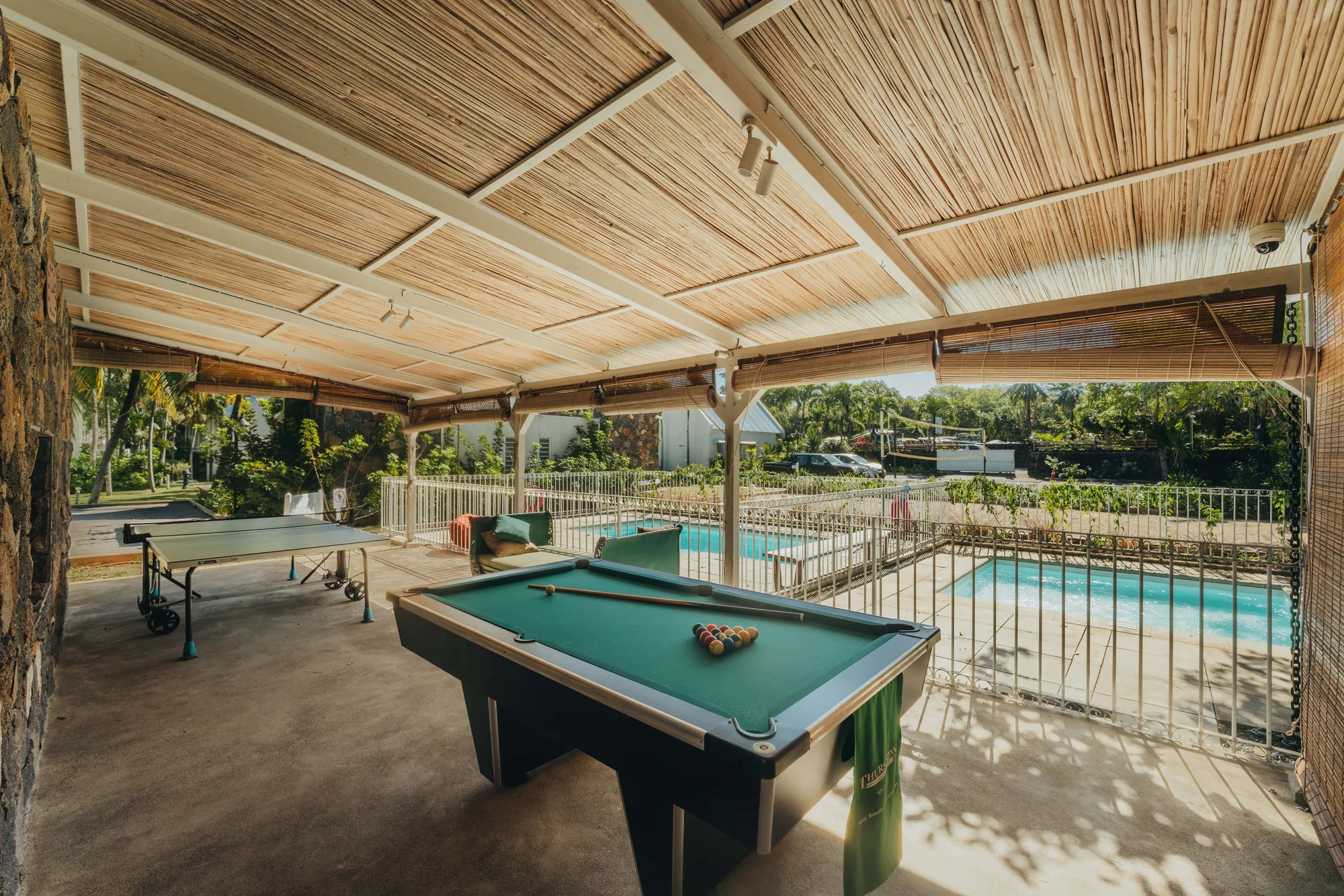 A covered games terrace with a pool table and table tennis beside the pool