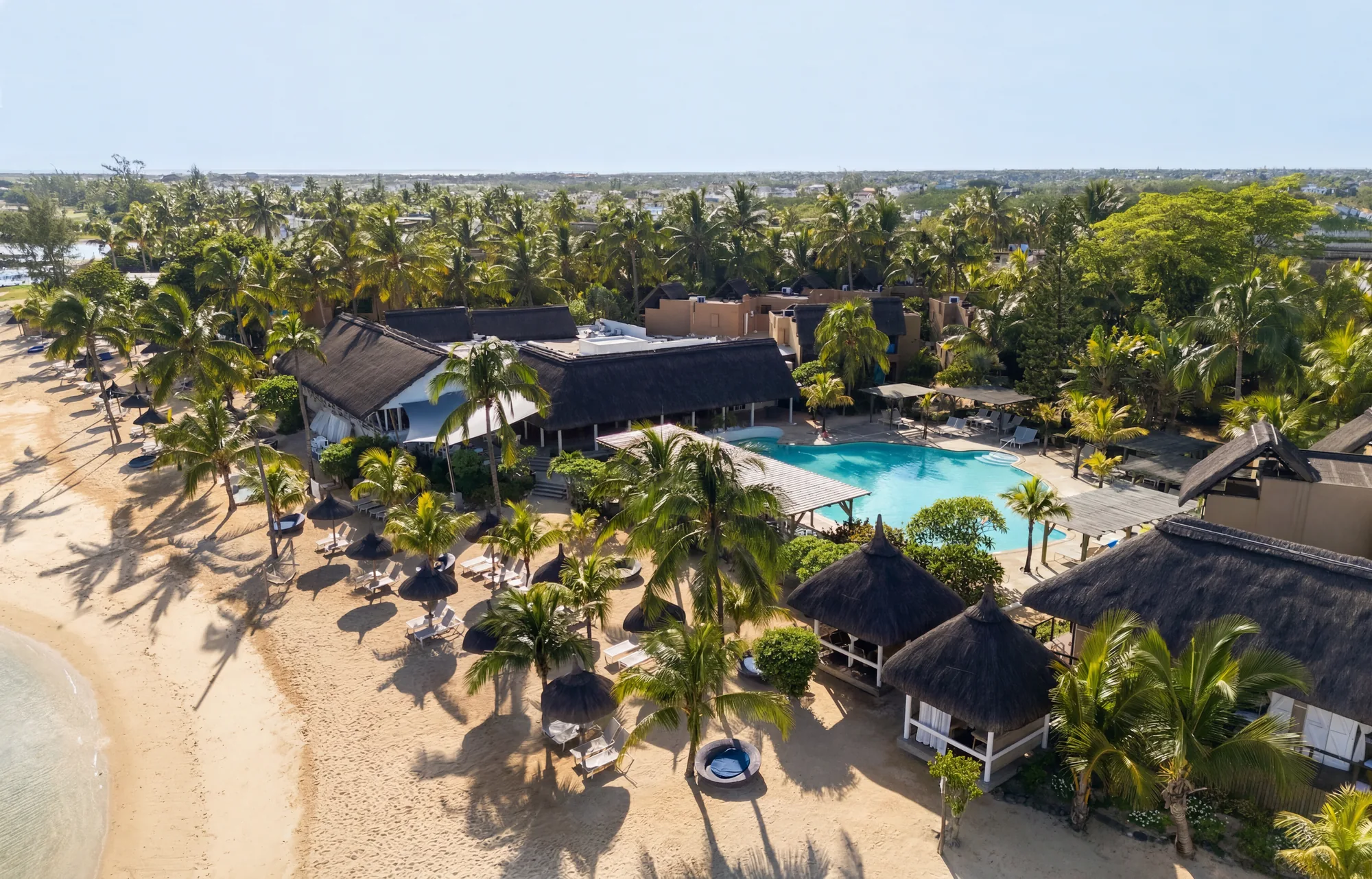 Aerial view of Veranda Pointe aux Biches, its thatched roofs and pool among palm trees beside the beach