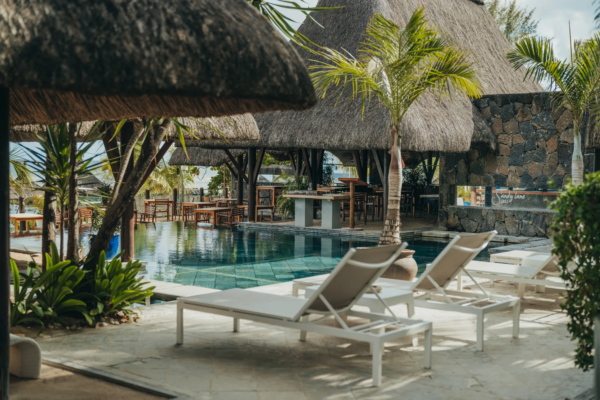 Loungers beside a pool in front of a thatched restaurant