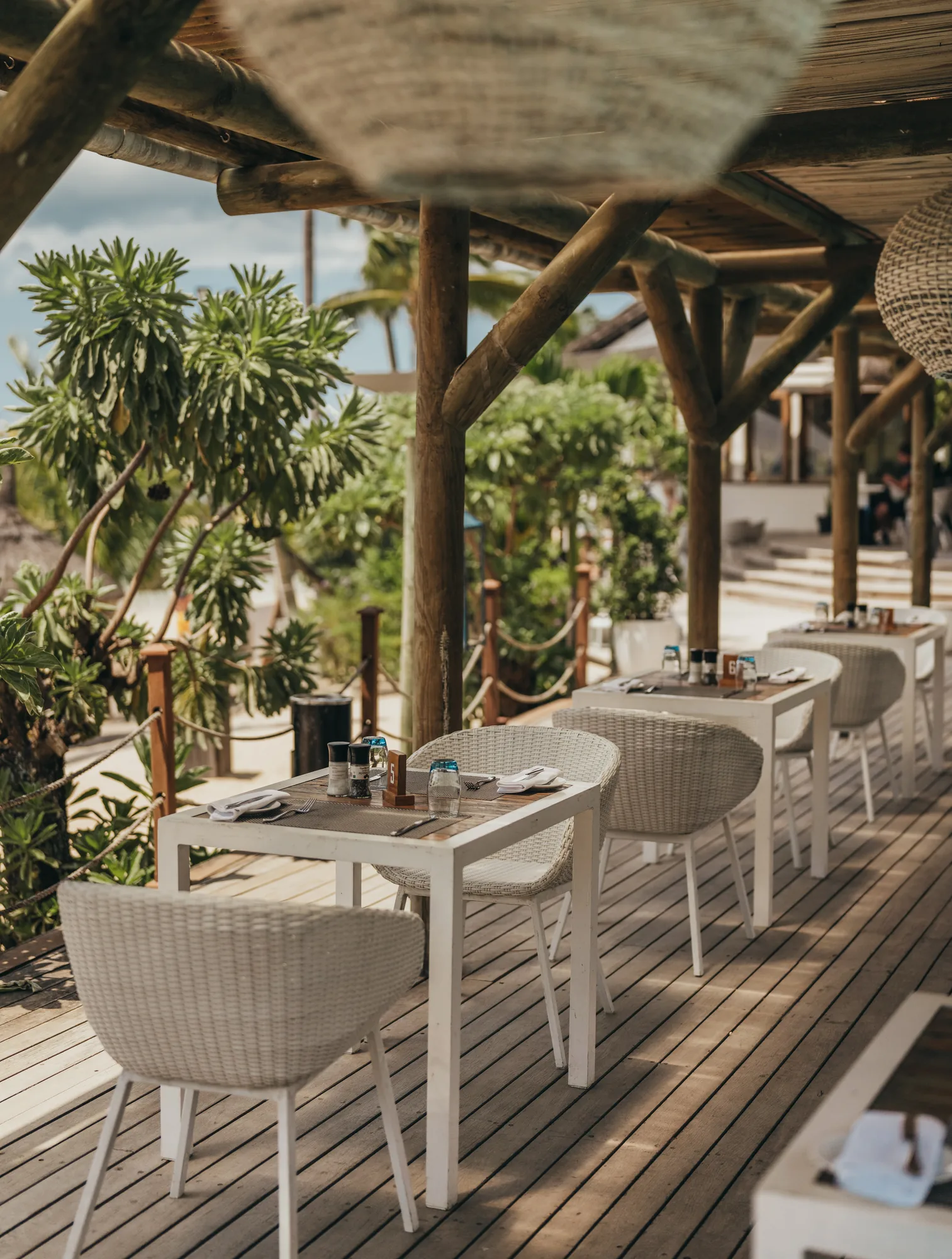 Restaurant tables along a deck under a thatched roof