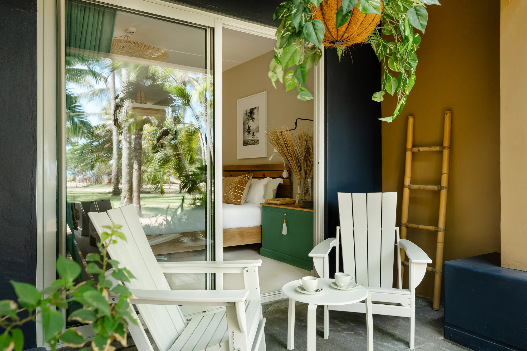 A balcony with white wooden chairs, looking onto palms