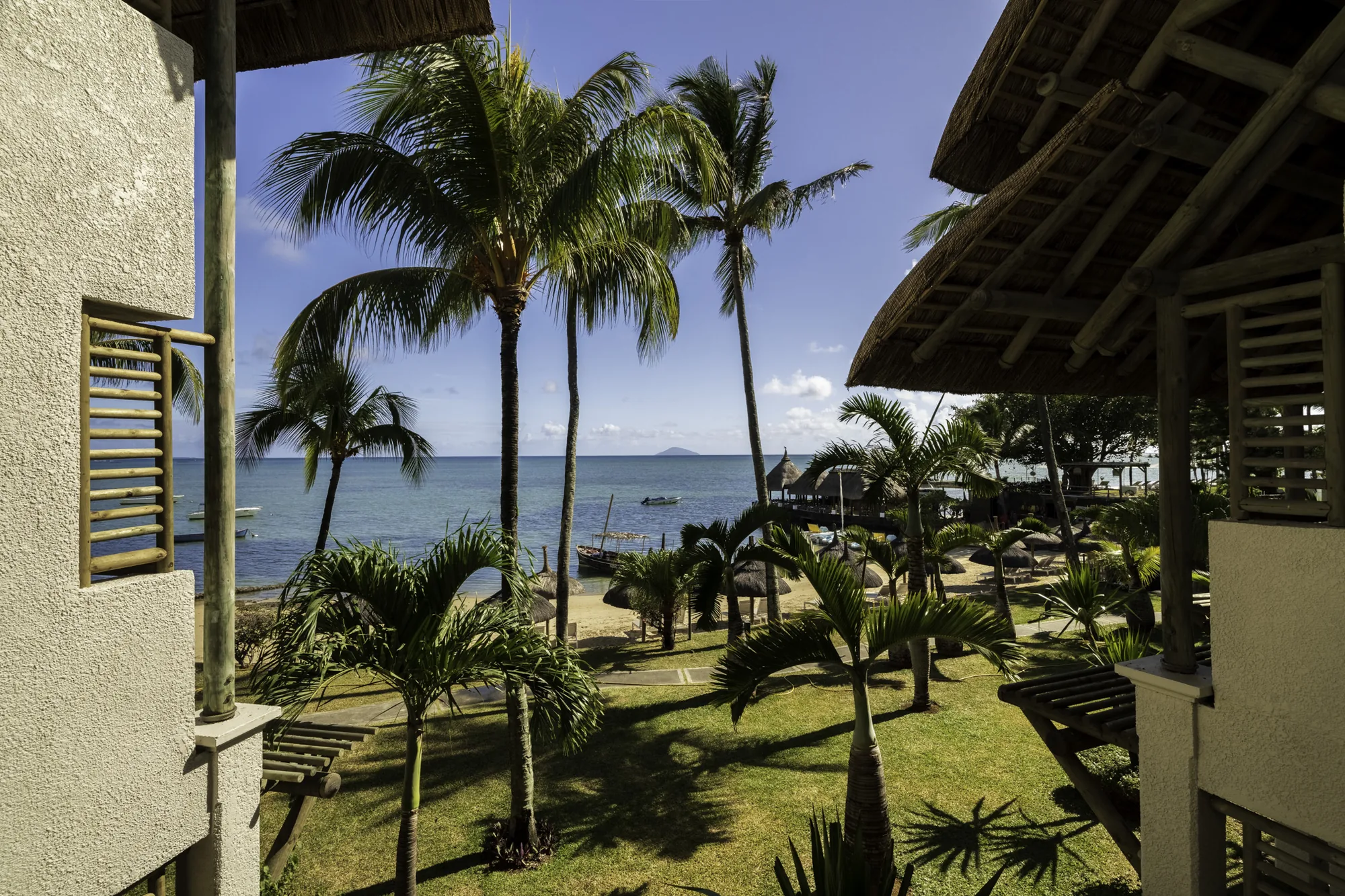 Palm trees and the lagoon seen from a balcony under a thatched roof