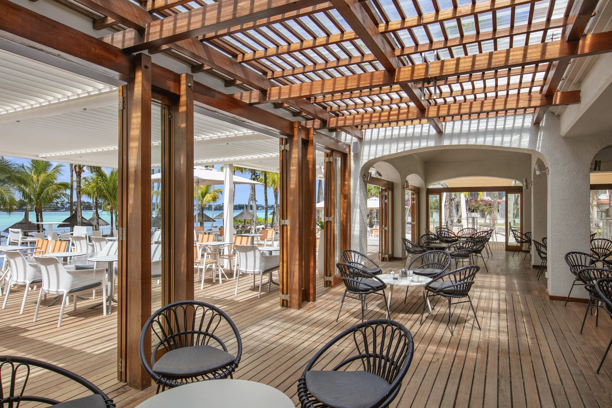 A restaurant terrace under a timber pergola, with black chairs and white tables