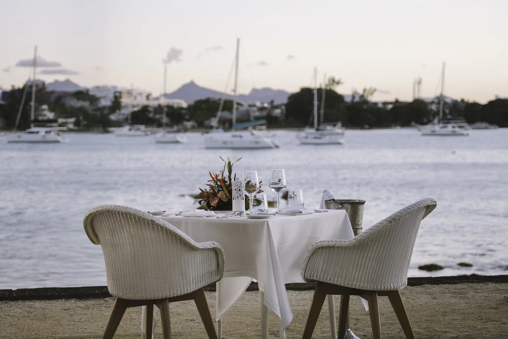 A table for two laid on the beach, facing a bay of moored yachts