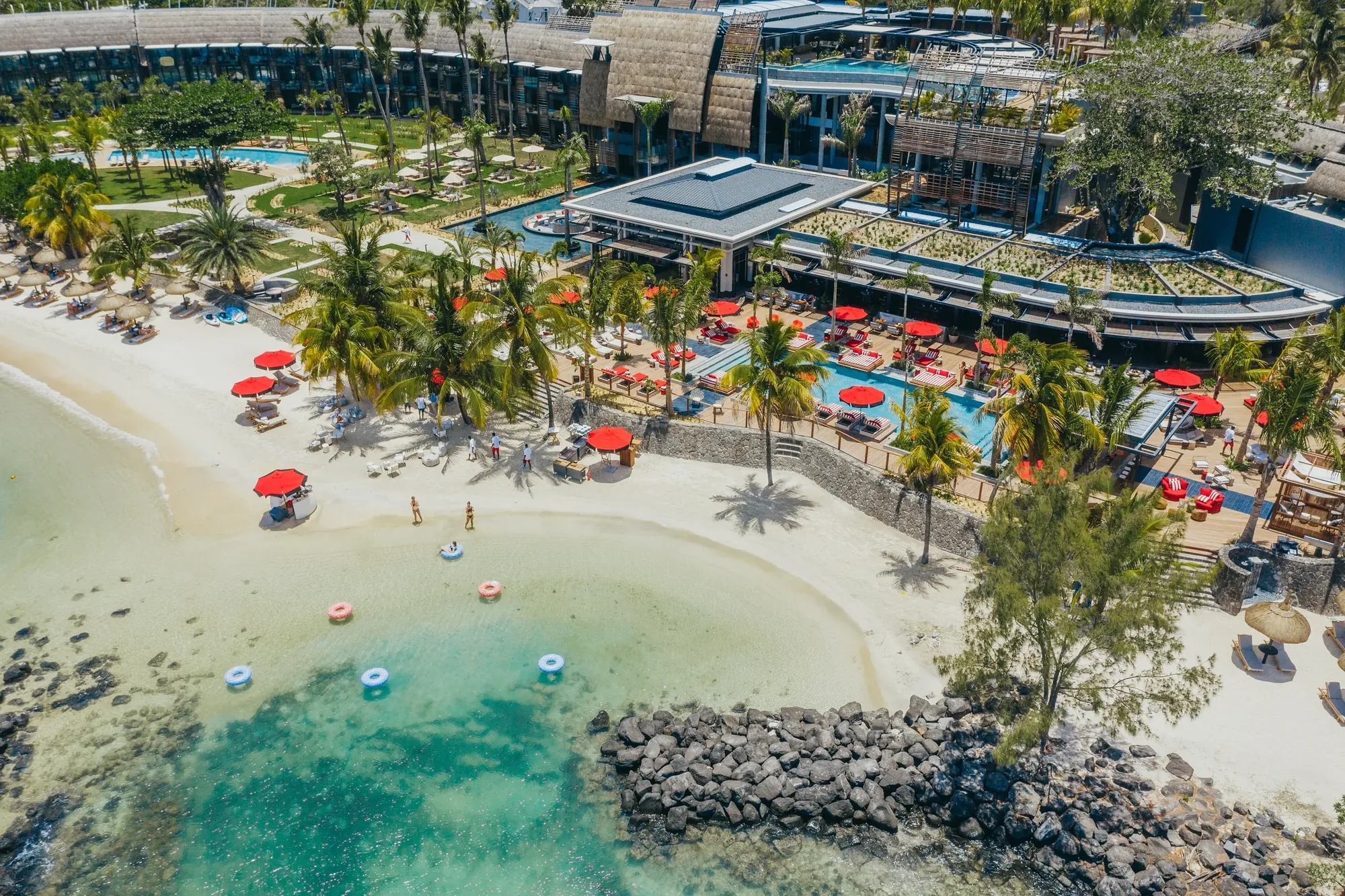 Aerial view of LUX* Grand Baie, its buildings and pool behind a small beach and lagoon