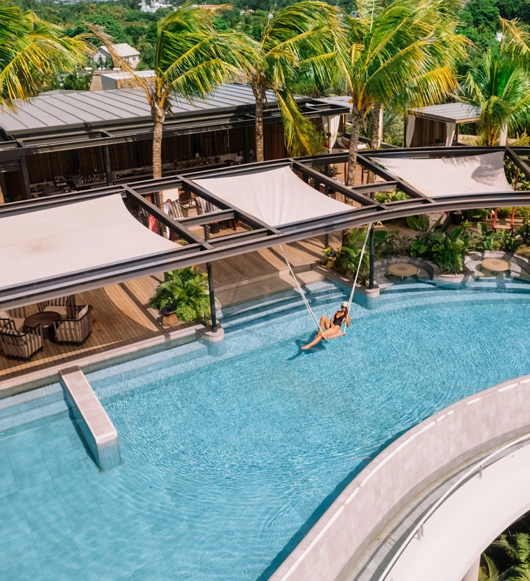 A swing over a curved pool, under shade sails