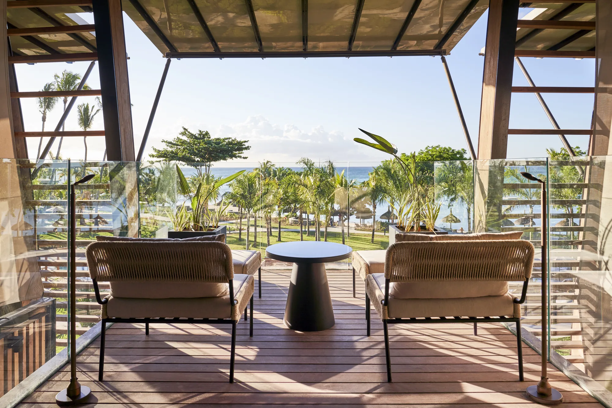 Two armchairs on a balcony looking over palm trees to the sea