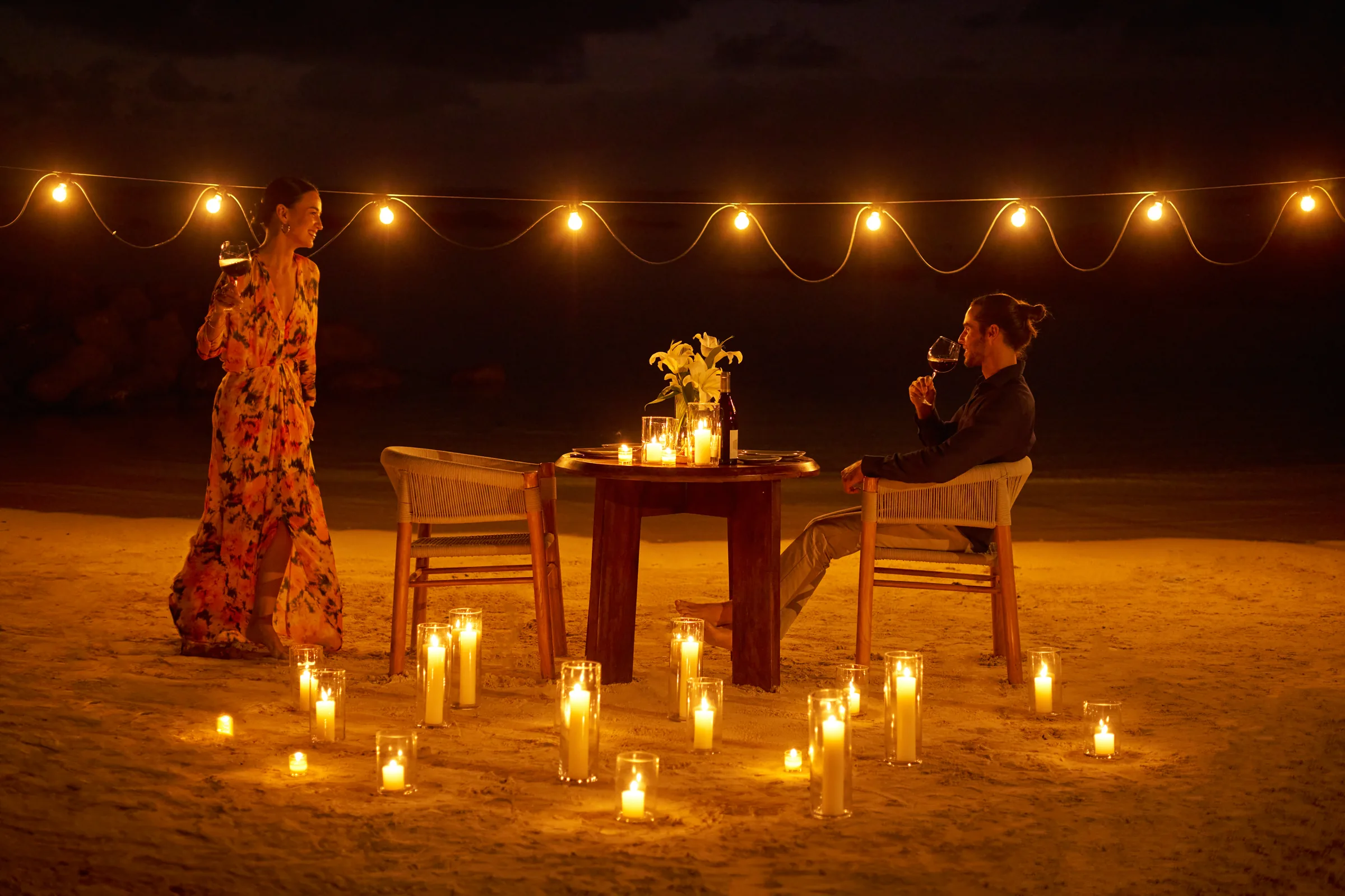 A couple at a candlelit table on the beach at night