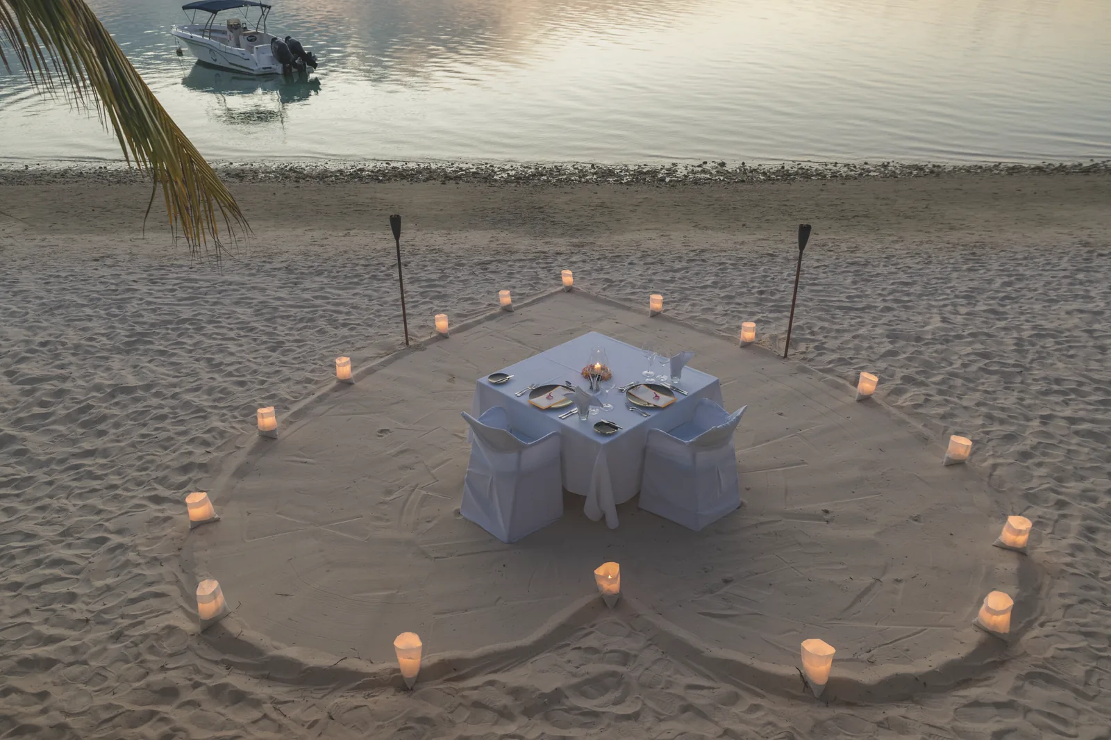 A candlelit table for two inside a heart drawn in the sand