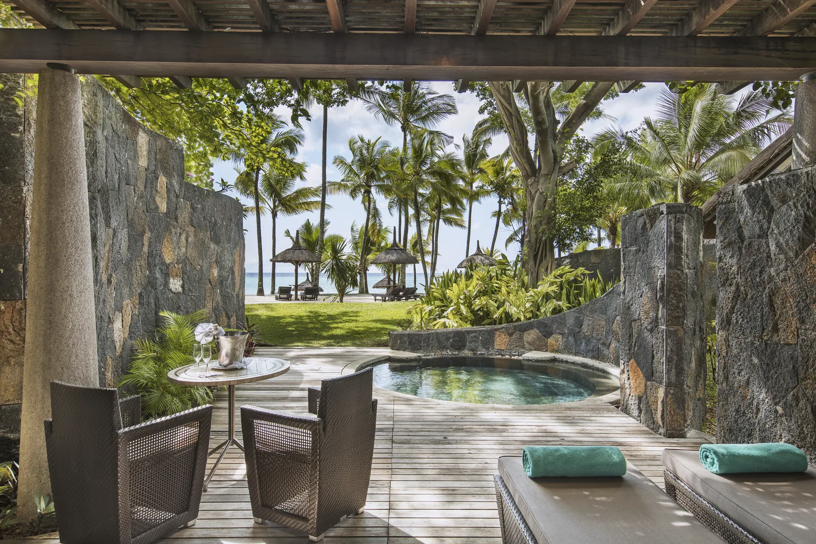 A villa terrace with a plunge pool and loungers between stone walls, looking to the beach