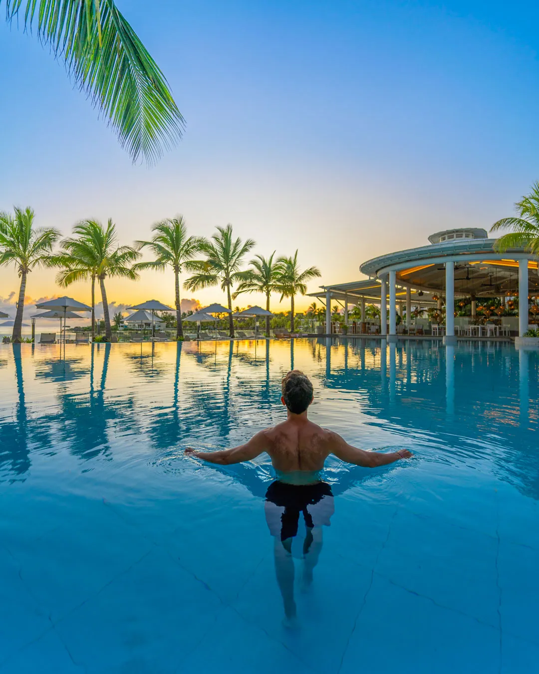 A guest standing in an infinity pool at sunset