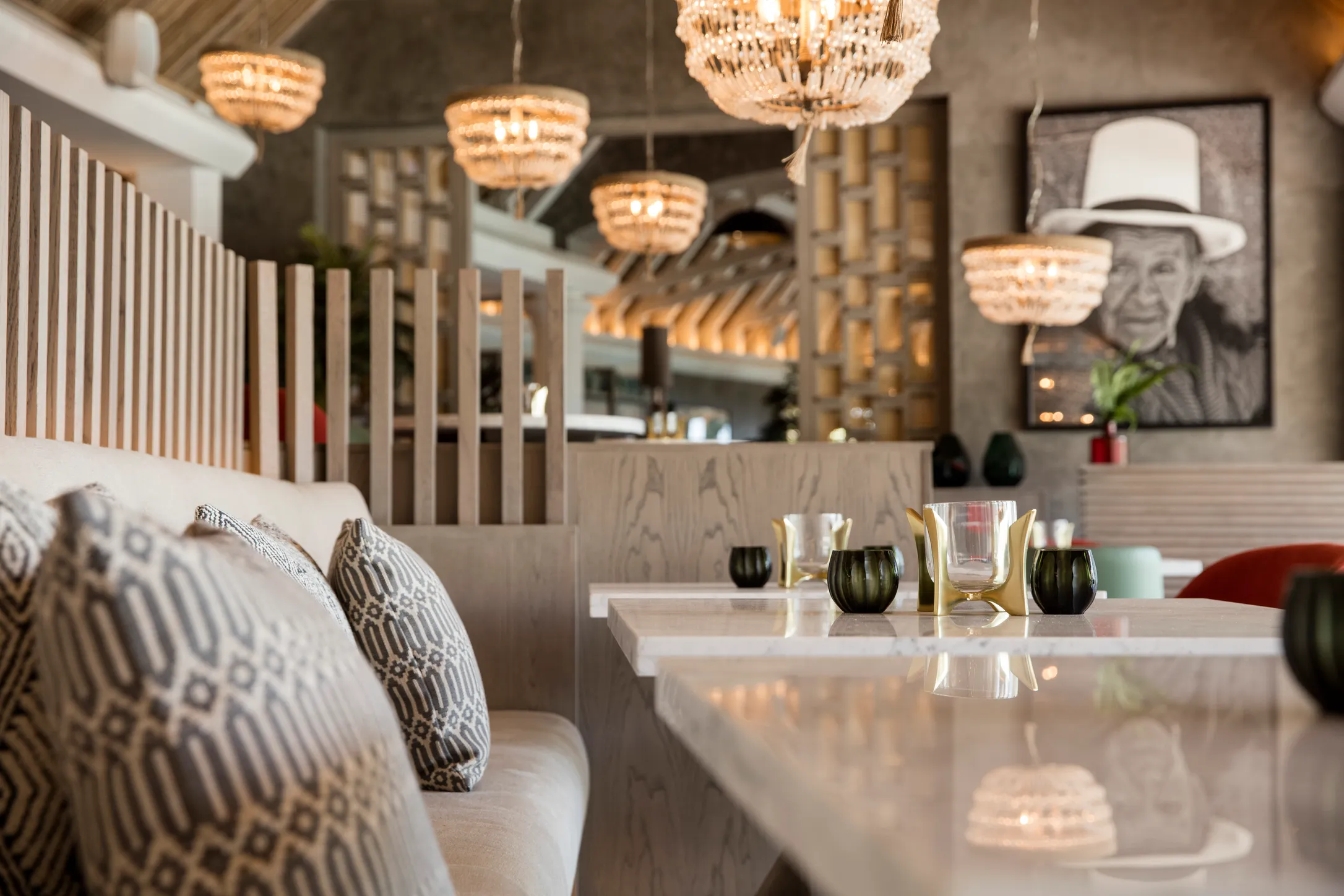 A bar with patterned cushions, pendant lights and a framed portrait on the wall
