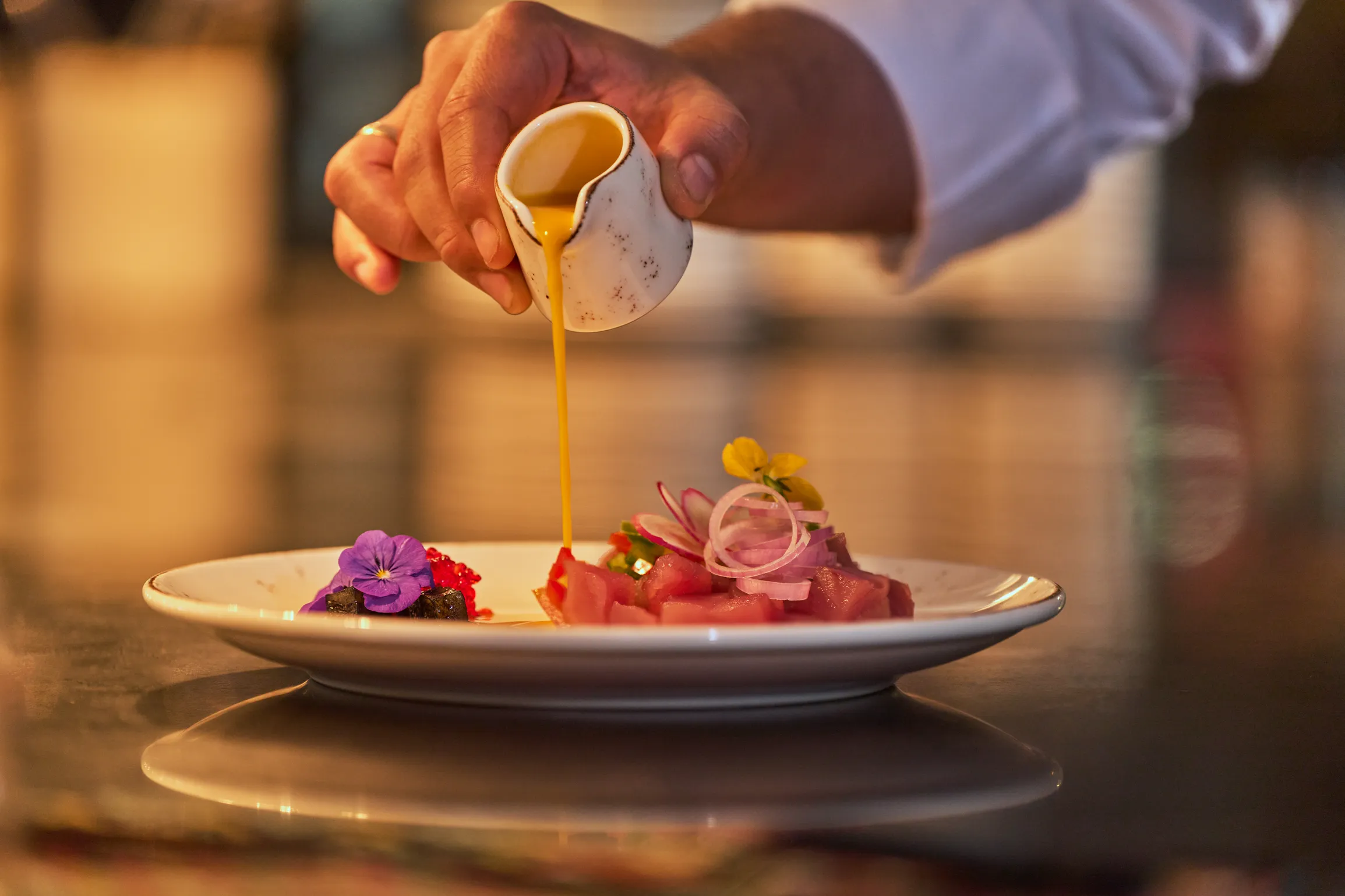 A sauce being poured over a plated dish