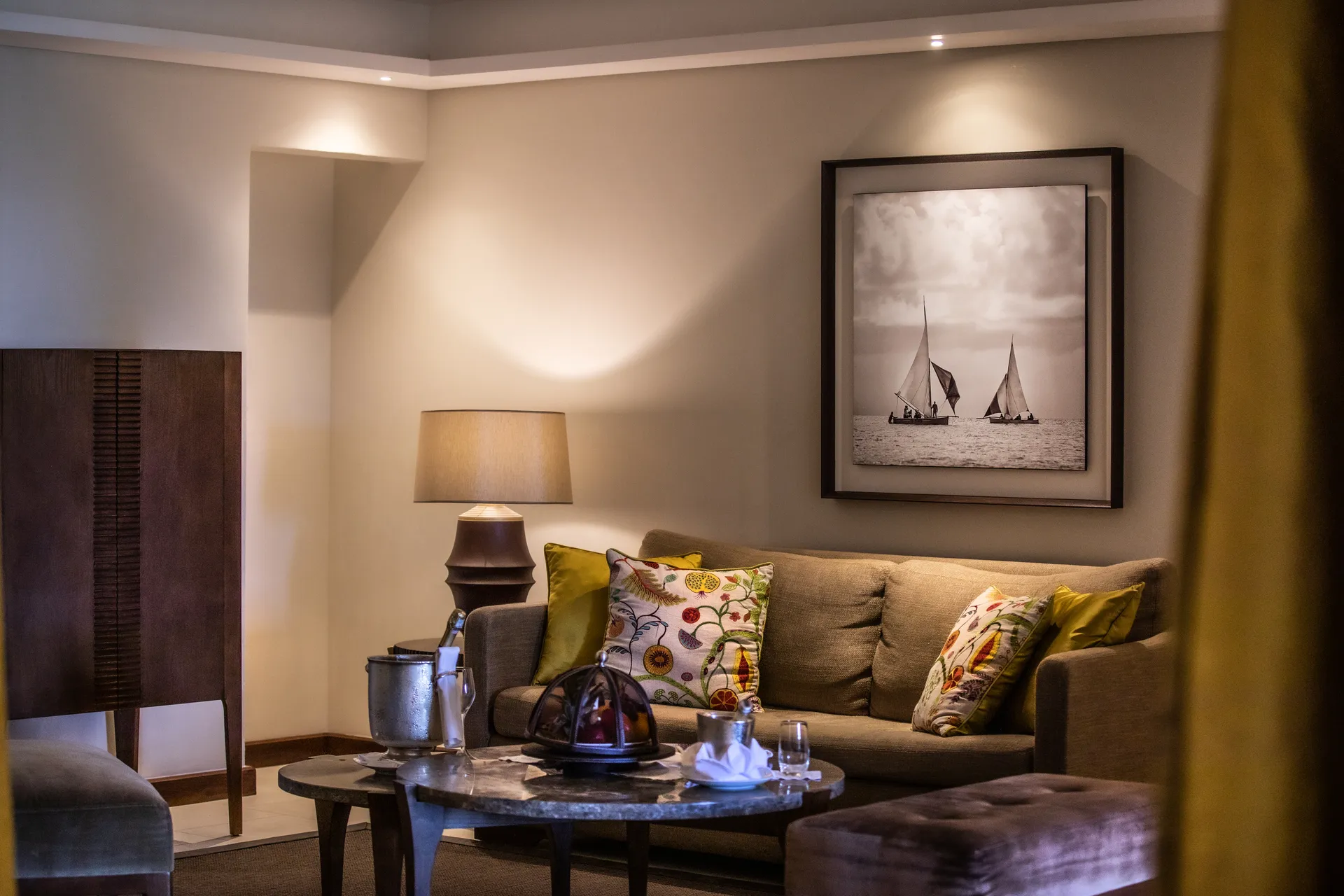 A sitting area with a sofa, cushions and a framed print of sailing boats
