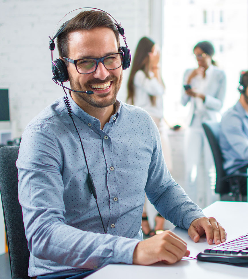 A photo of a customer service representative sitting at a desk, wearing a headset, and smiling at the viewer.