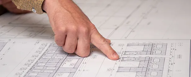 Close-up of a hand pointing at detailed architectural blueprints, highlighting a specific section of a technical drawing with measurements and structural details.