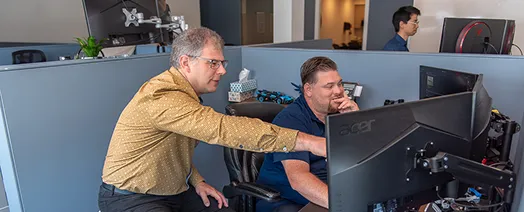 Two colleagues collaborating at a computer, with one pointing at the screen while the other looks on attentively.